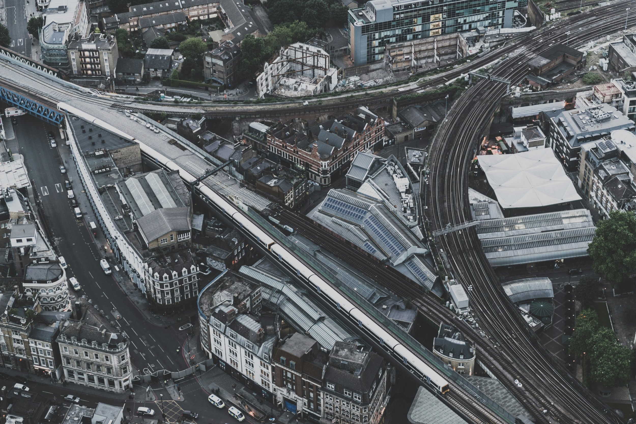 An aerial view of a dense urban cityscape featuring multiple railway tracks, a train, and a mixture of old and modern buildings, with roads and green trees.