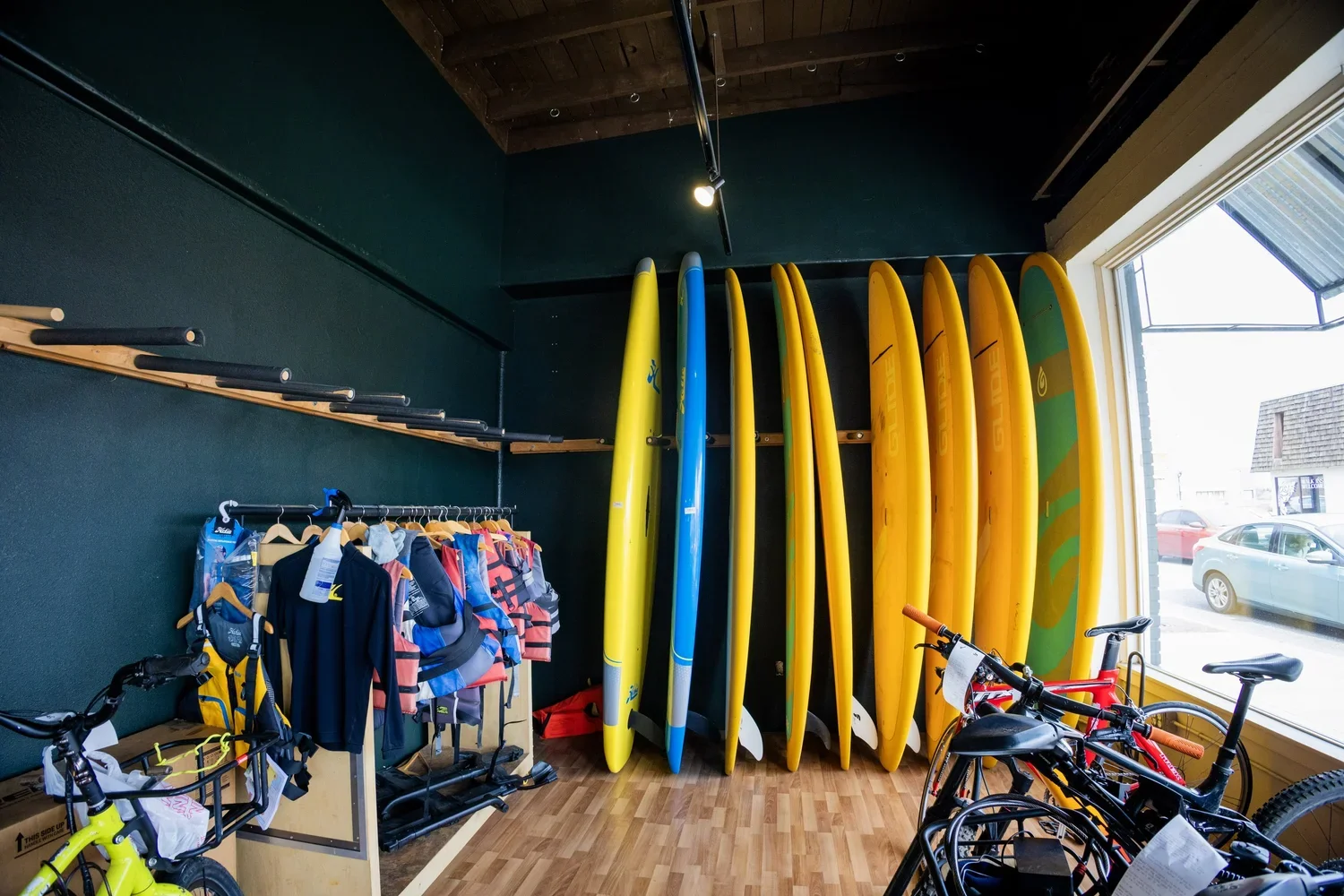 Indoor surfboard shop with surfboards hanging on a wall, fishing gear hanging on a rack, and bikes in the foreground.
