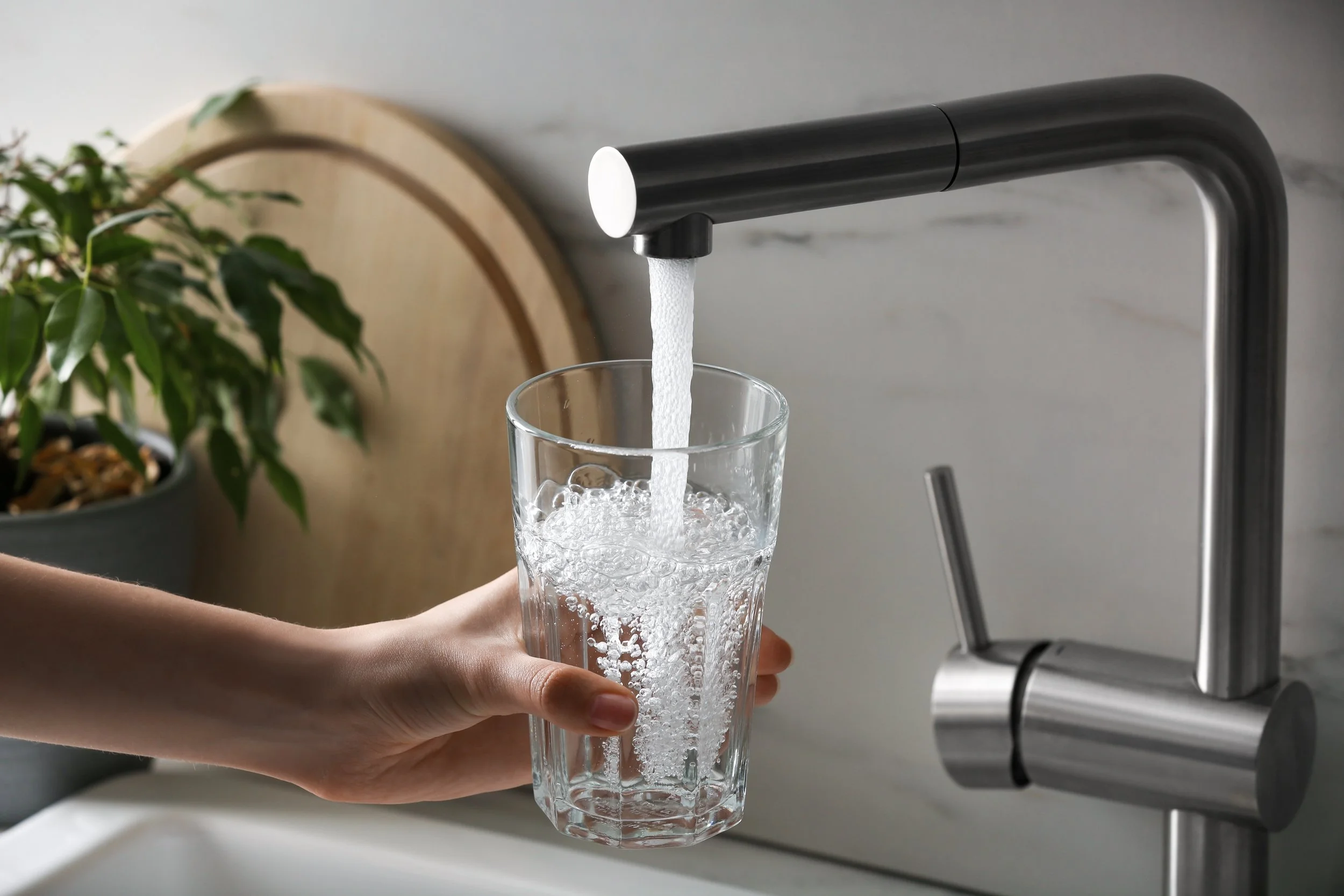 Hand filling a clear glass with water from a modern faucet in a kitchen.