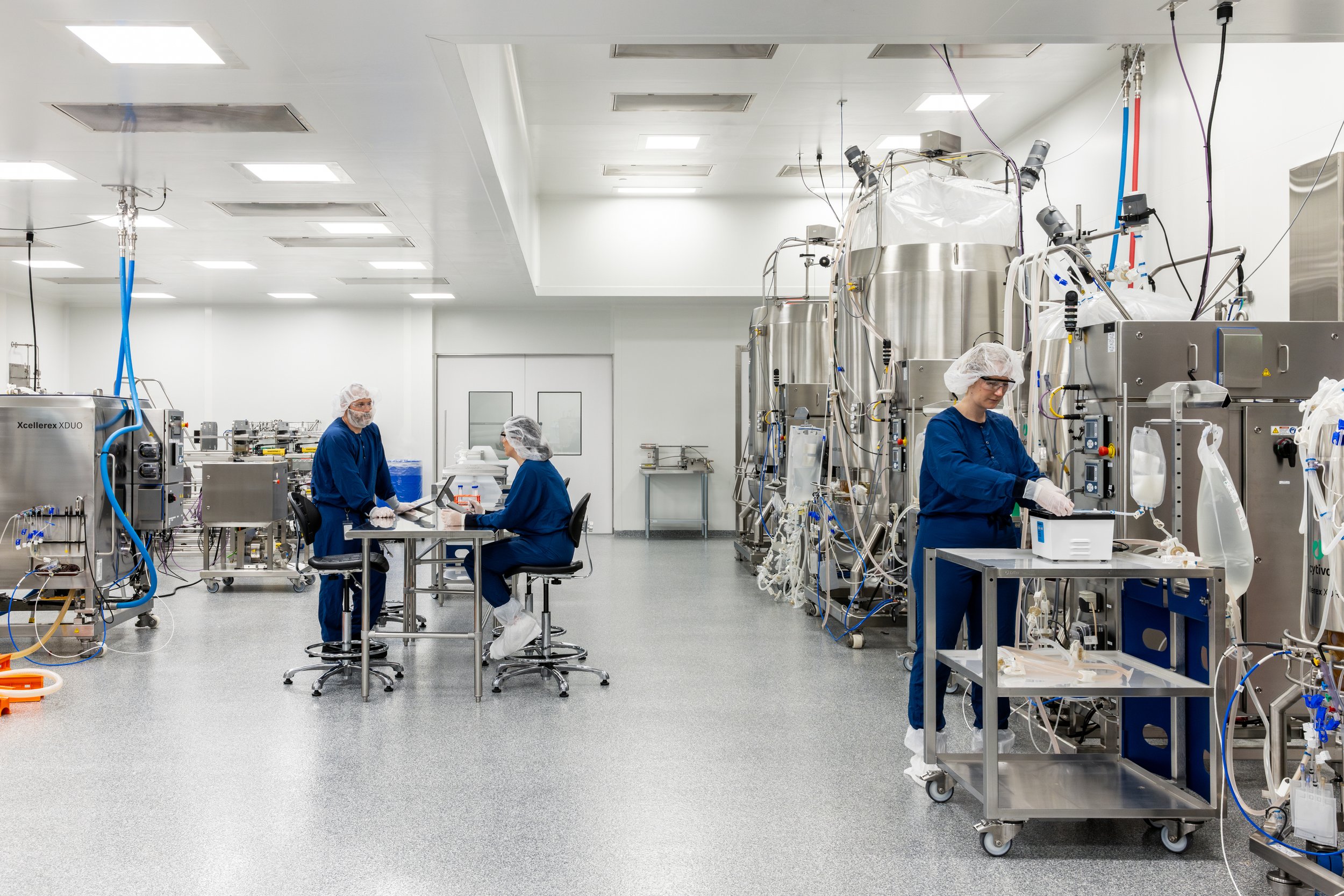 Scientists in a cleanroom working with large industrial machinery, wearing protective gear like hairnets, gloves, and lab coats.