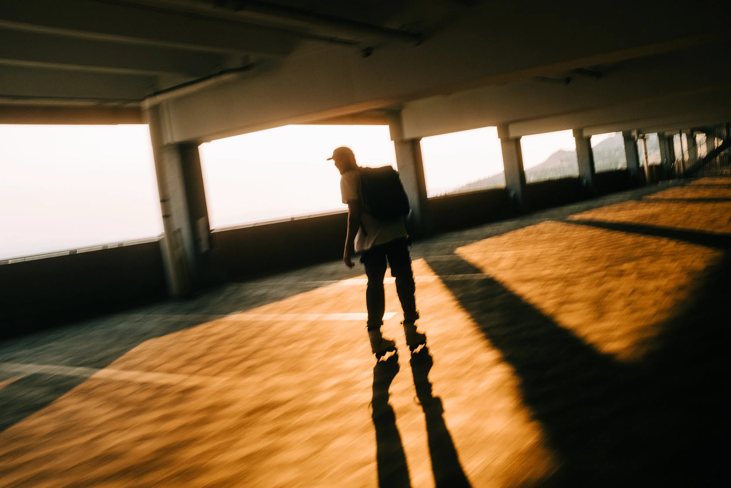 A person walking in an open parking garage during sunset, creating long shadows on the ground.
