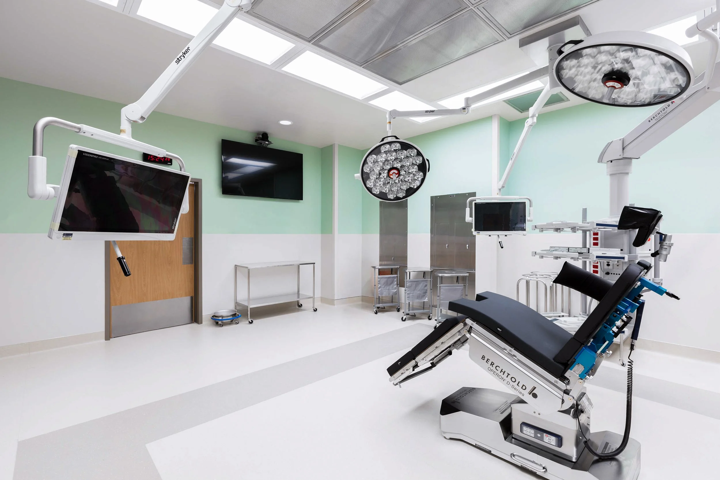An operating room with medical equipment, including surgical lights, monitors, and a surgical bed, in a hospital setting.