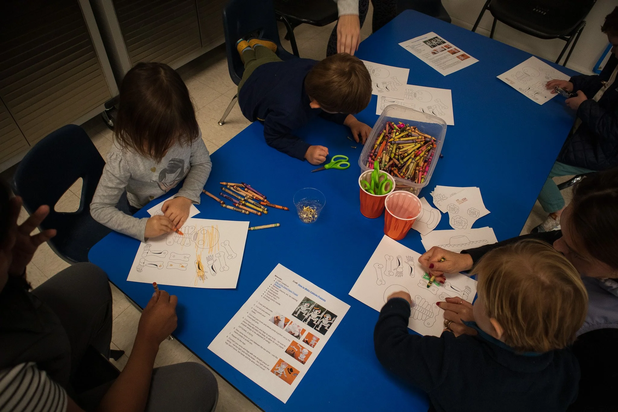 Children sitting around a blue table, coloring and drawing on paper with Crayola crayons.