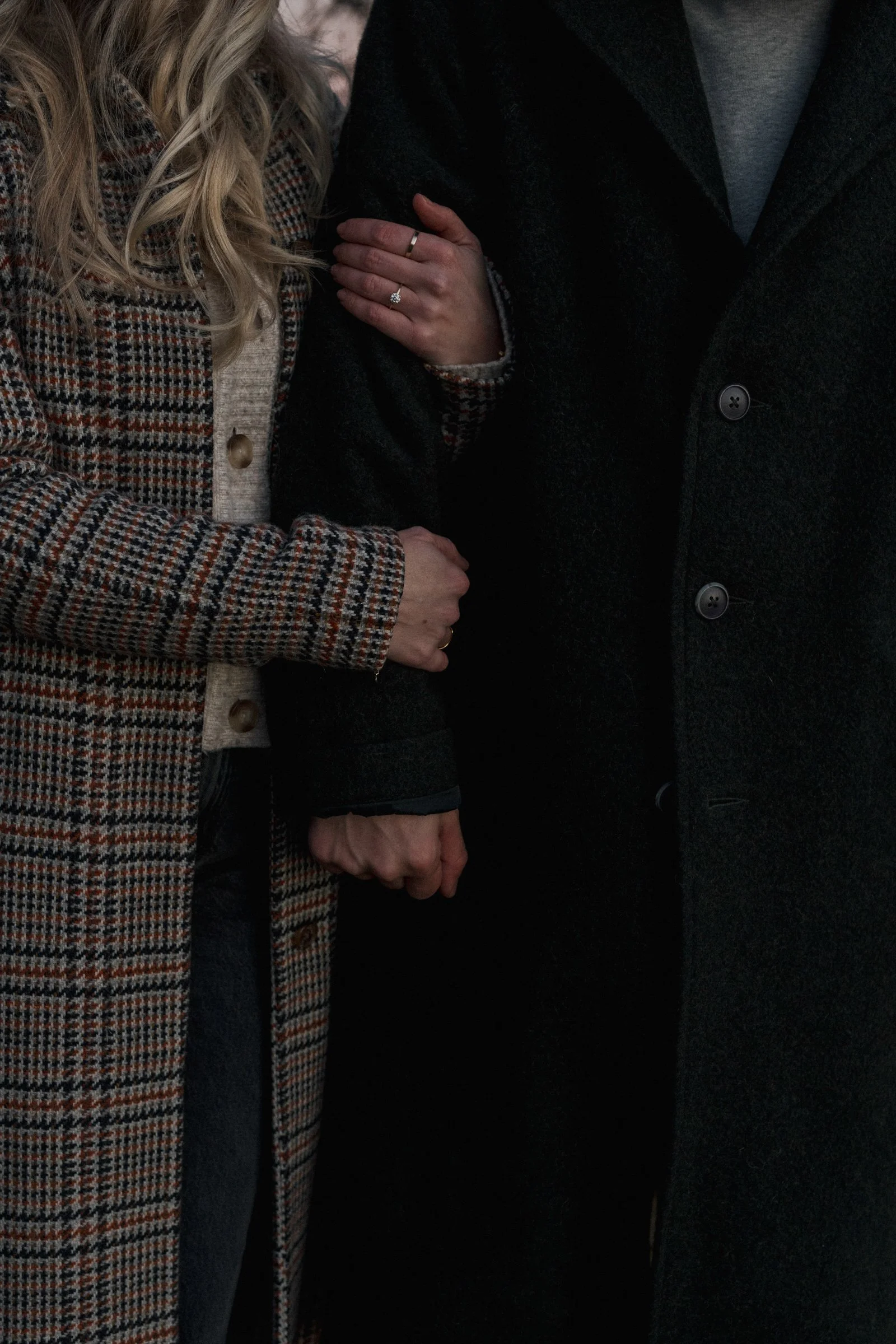 Close-up of a woman holding the arm of a man, both dressed in winter clothing, with emphasis on their hands and attire.