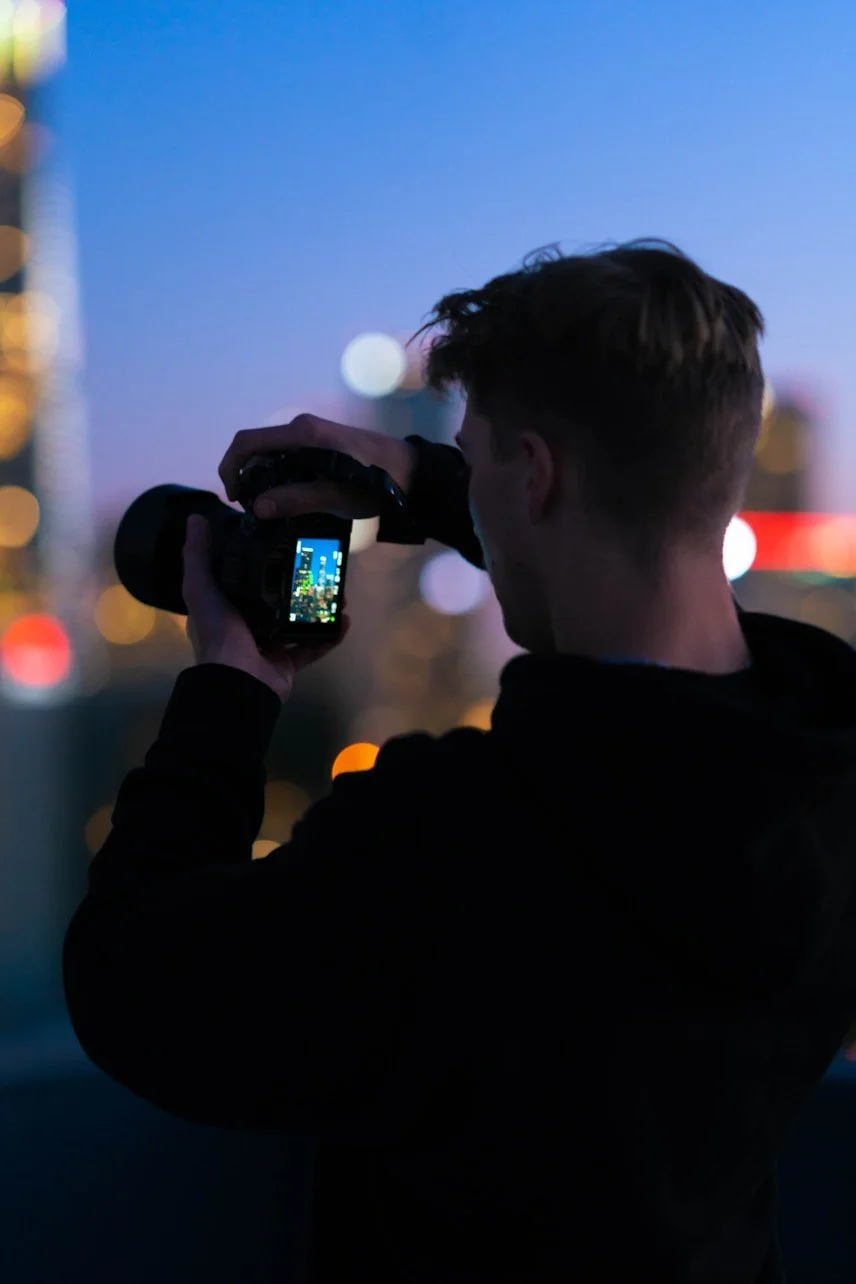 Jeune homme en silhouette qui prend une photo d'une scène urbaine nocturne avec un appareil photo numérique.