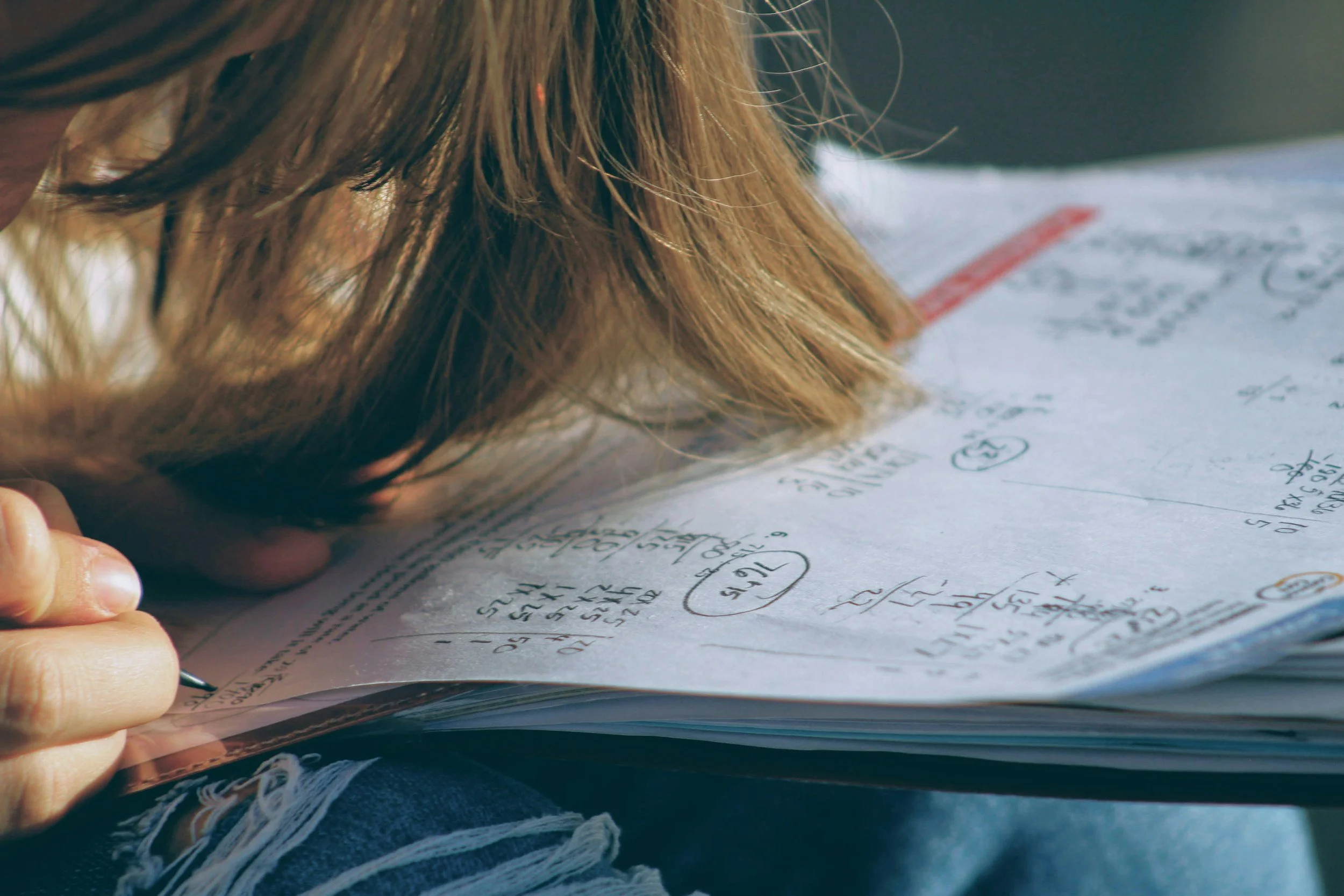 Person studying or doing homework, writing on a paper with notes and calculations.
