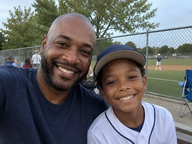 Father and young baseball player smiling together at a youth baseball game