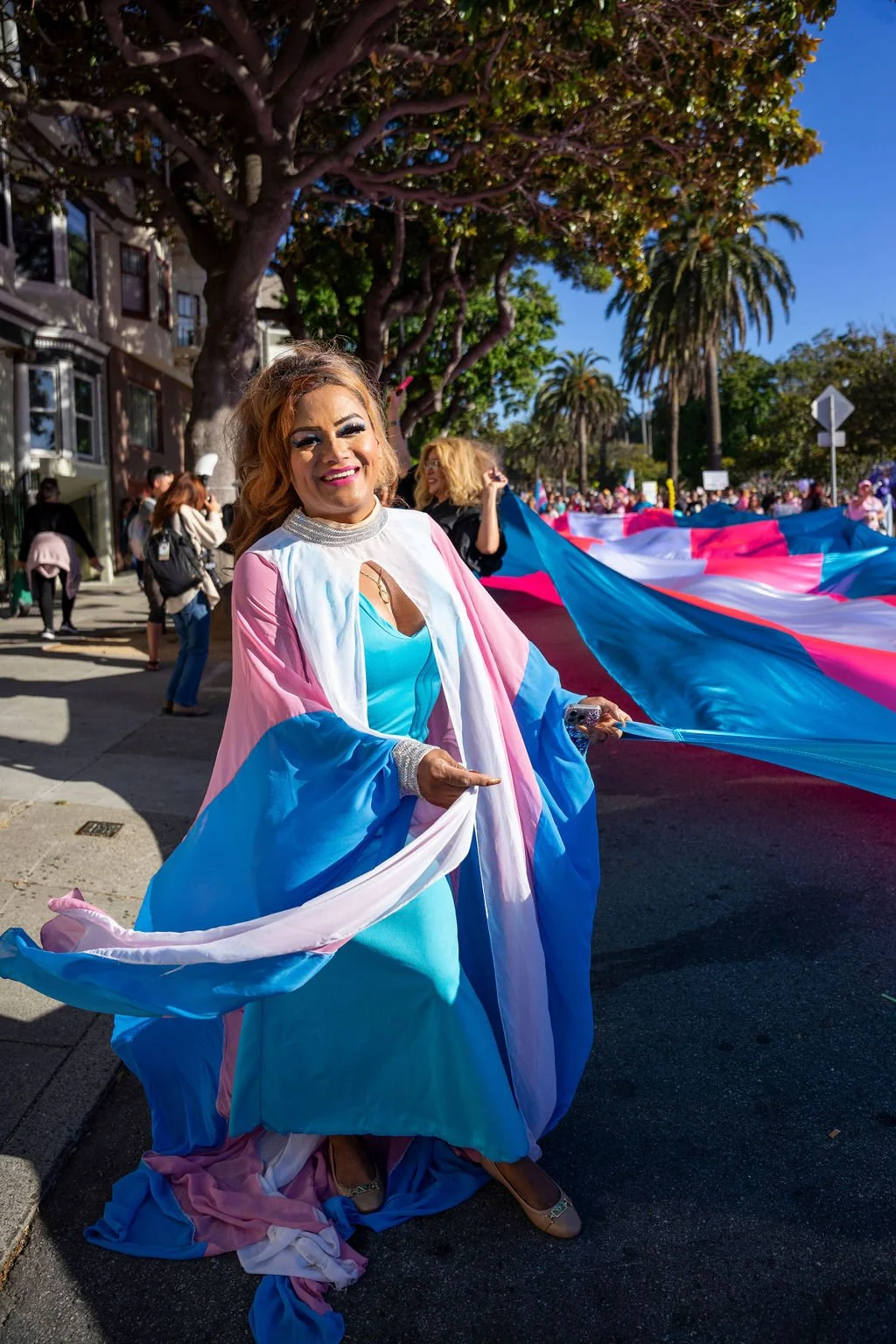 Sthefany G., El/La's Program & Outreach Manager, in a pink, blue, and white trans flag cape at the 2025 Trans March.