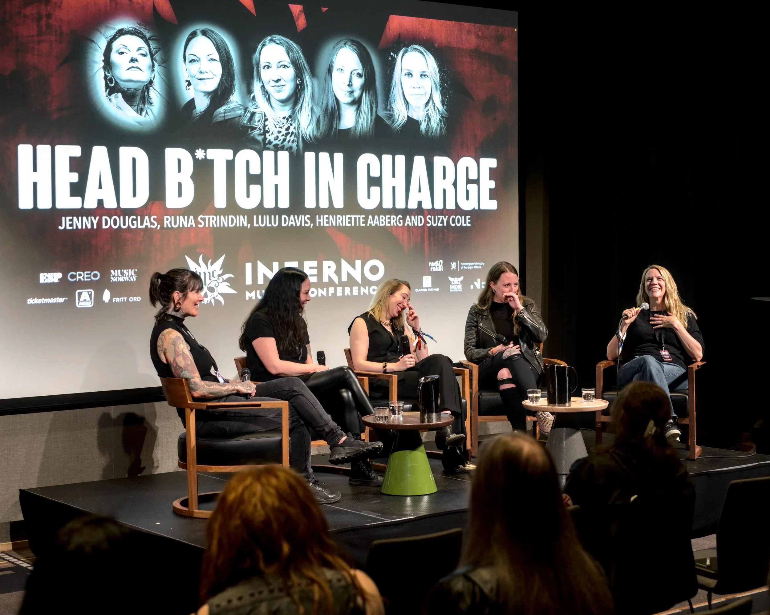 Panel discussion at the Inferno Feminist Music Conference, featuring five women on stage with a large screen behind them displaying the conference title and guest names.