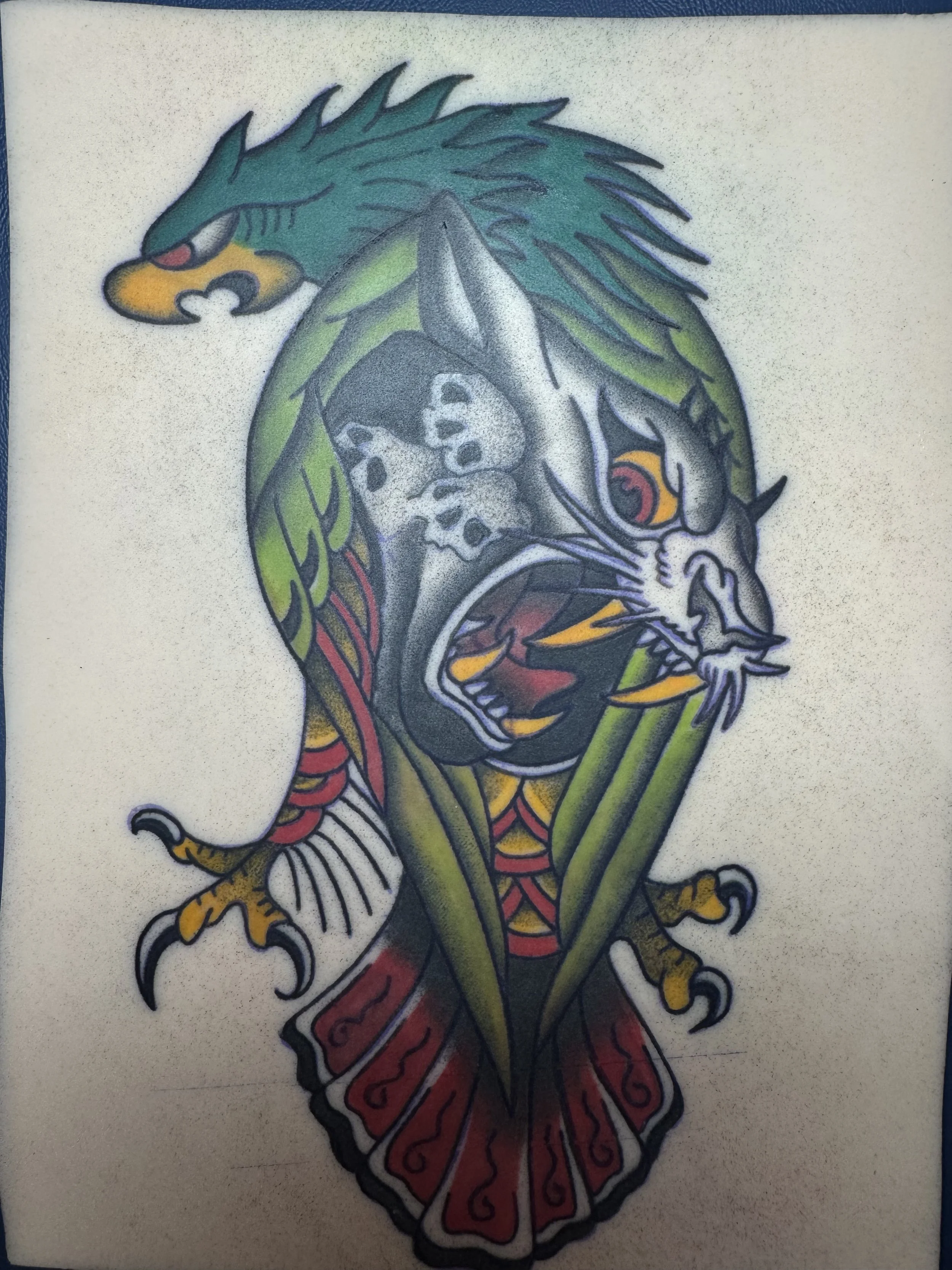 Tattoo of a fierce animal hybrid with elements of a lion and a bird, featuring vibrant colors such as green, yellow, red, and black.