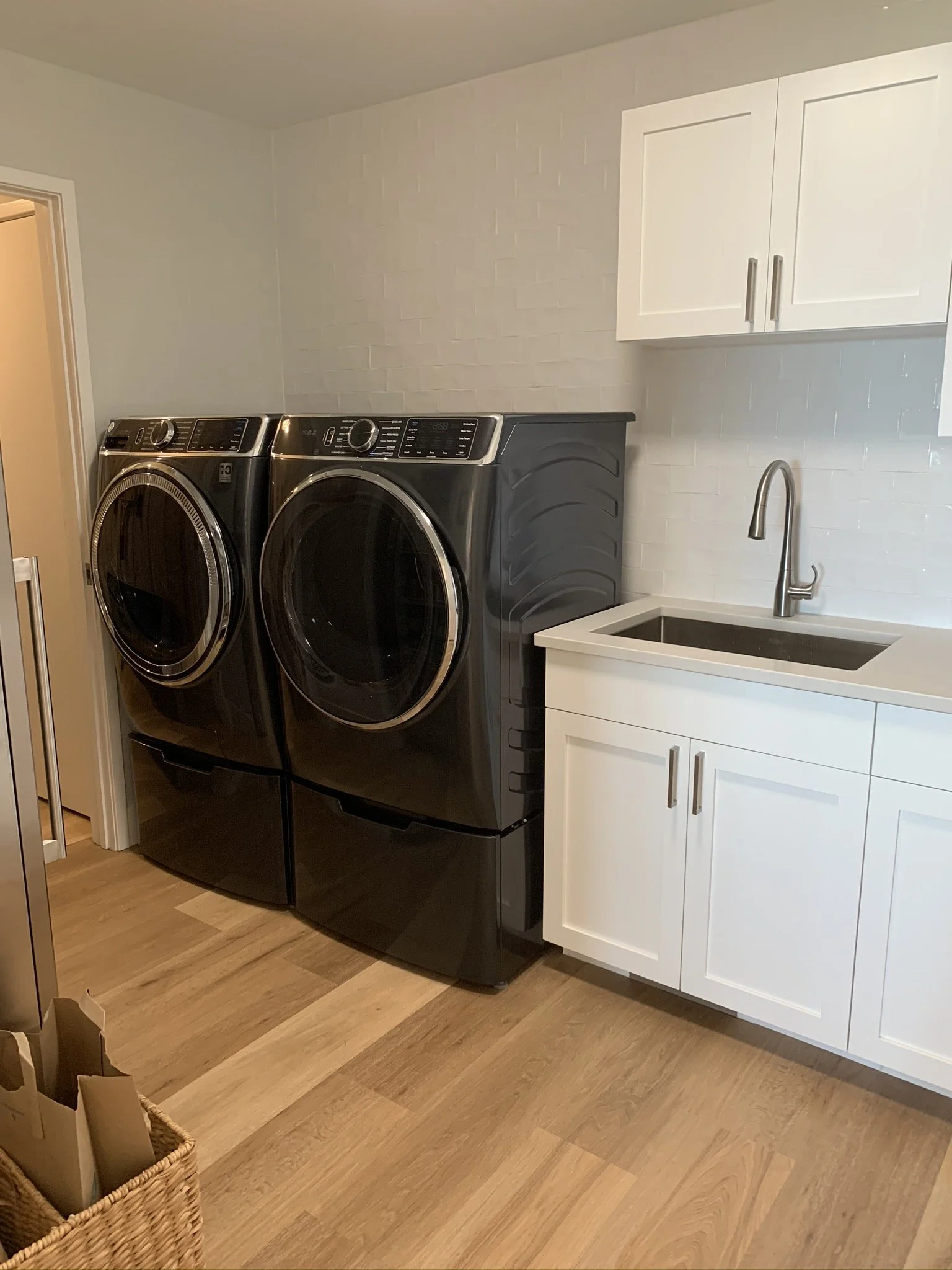 A laundry room with a black front-load washer and dryer, white cabinets above the sink, and hardwood flooring.