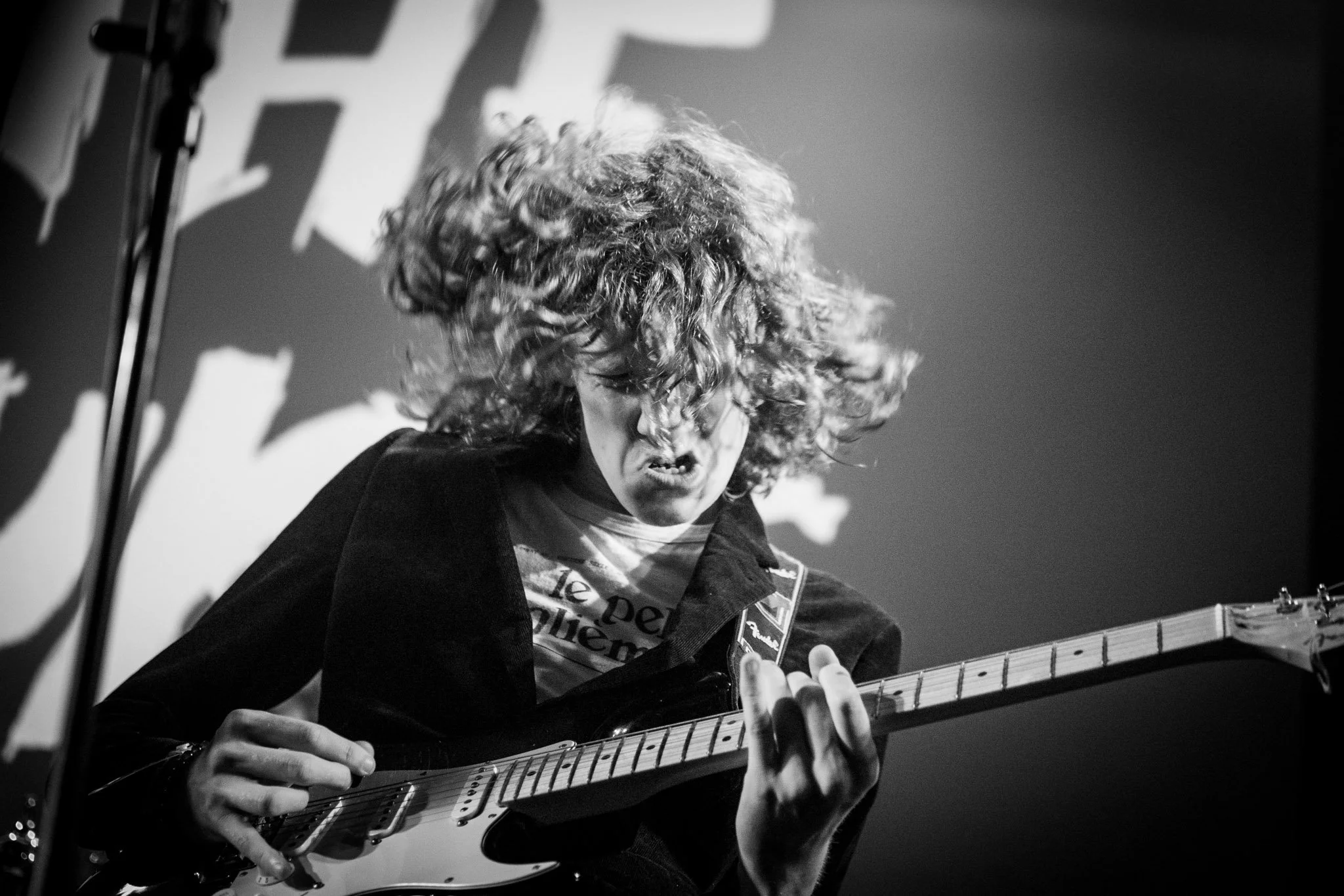 A person playing an electric guitar on stage with long curly hair covering their face, expressing intense emotion.