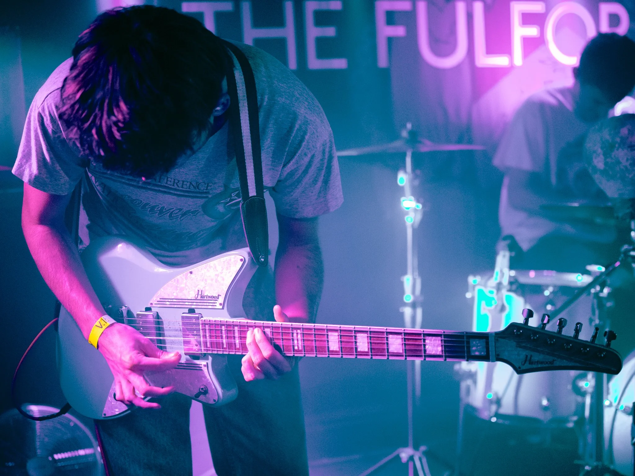 Musician playing an electric guitar on stage during a live music performance with neon lighting.