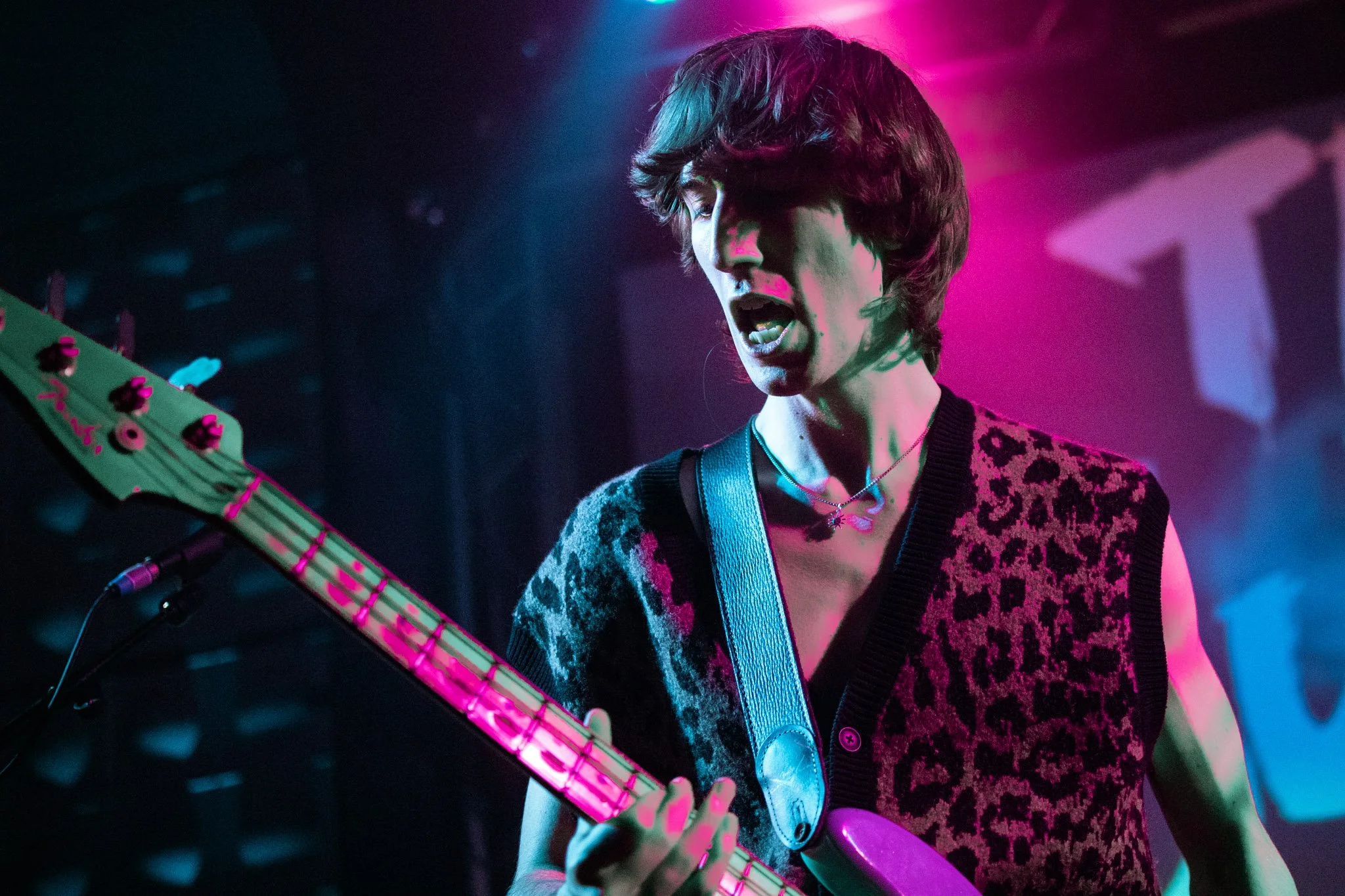 Female musician playing an electric guitar on stage with colorful pink, blue, and purple lighting.
