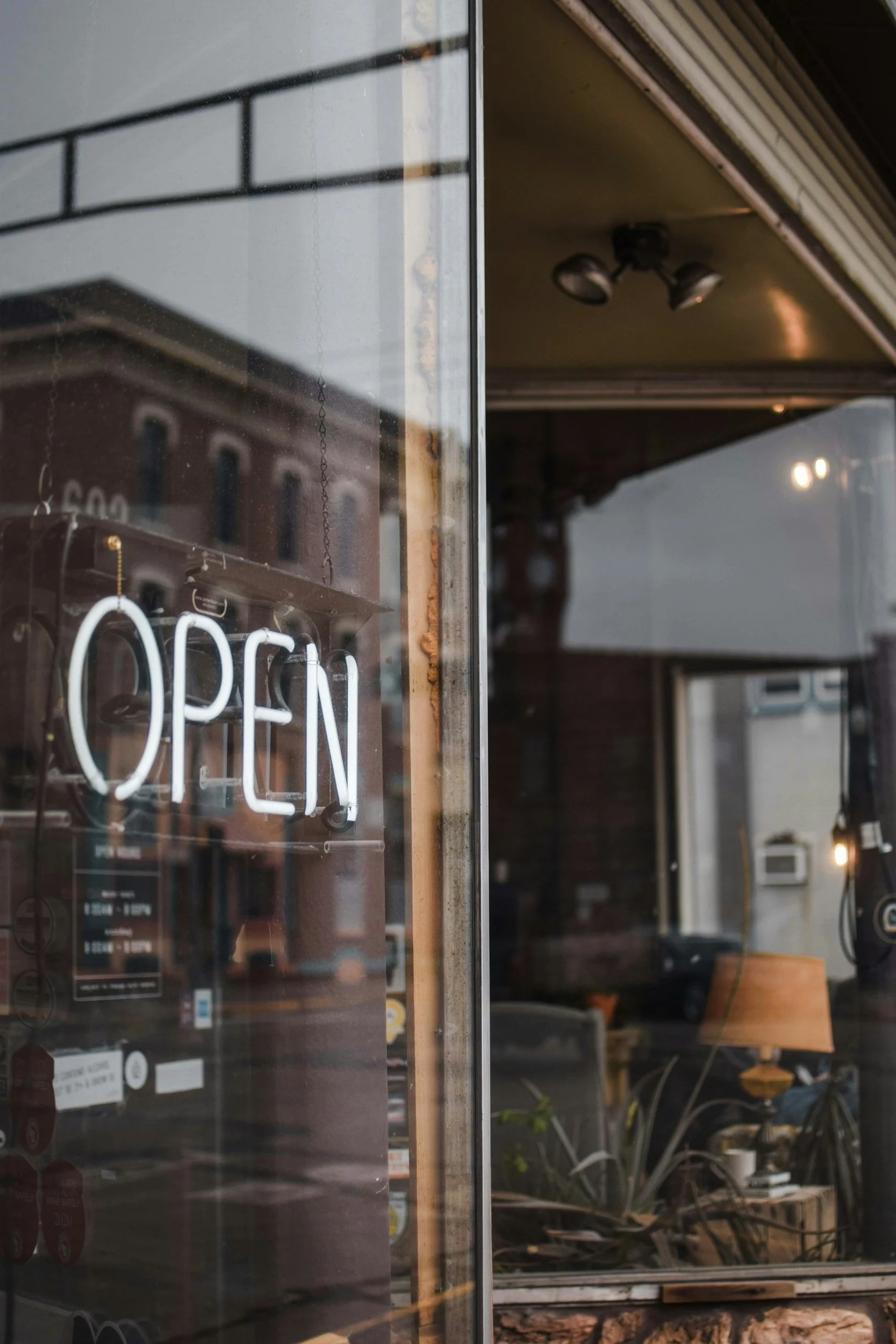 A glass storefront window with a neon 'OPEN' sign hanging inside. The interior features furniture and warm lighting.