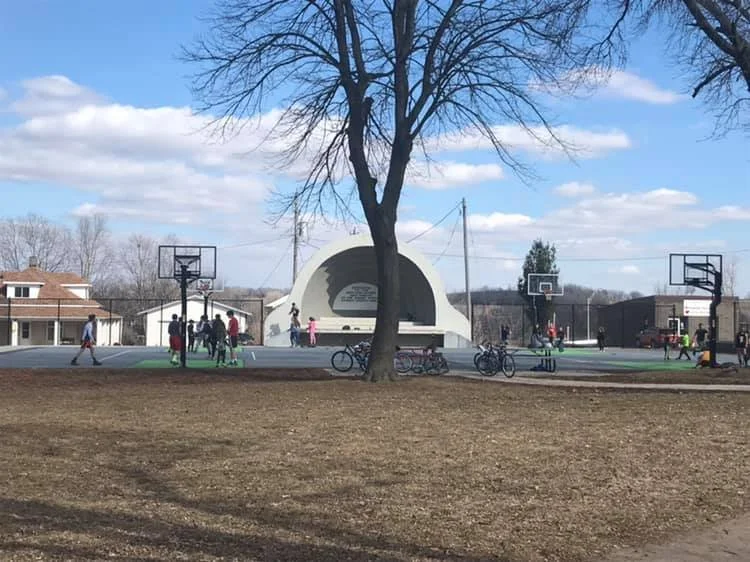 Logan city park with children riding bikes and playing on basketball court in front of an amphitheater.