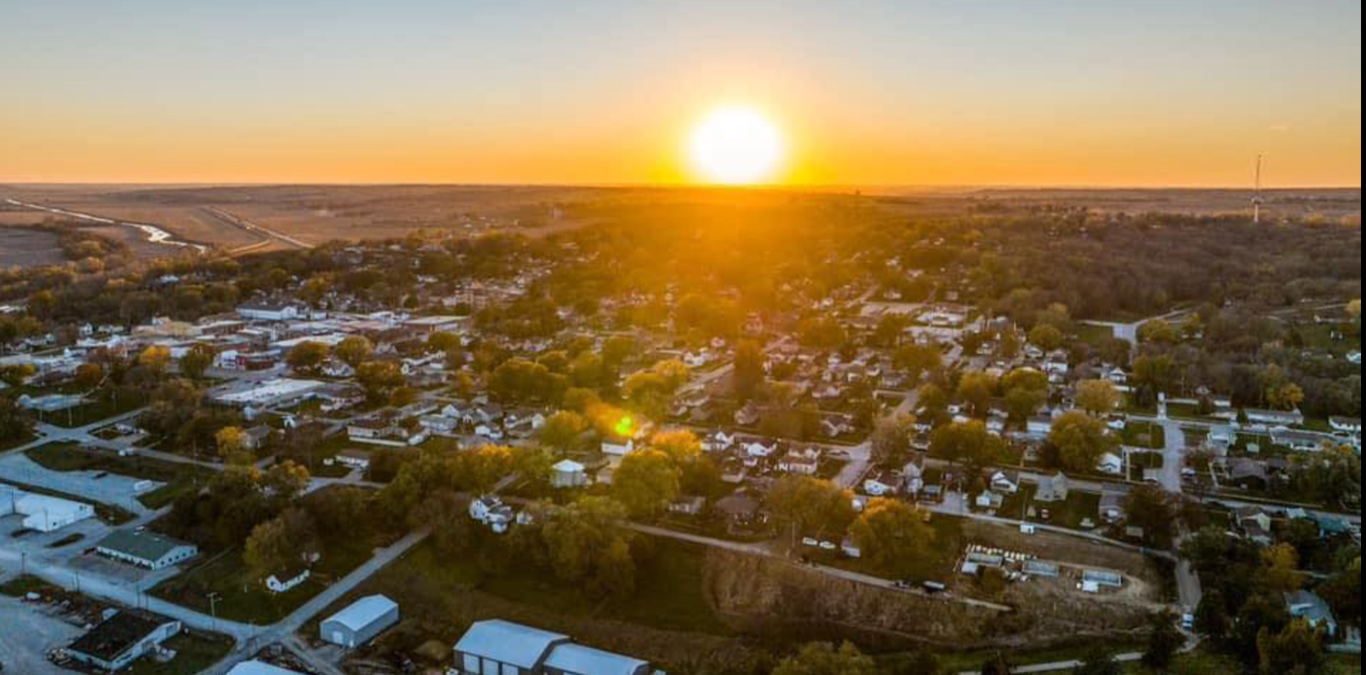 Aerial view of Logan, Iowa, at sunset, with residential houses, trees and our beautiful courthouse bathed in warm orange and yellow light.