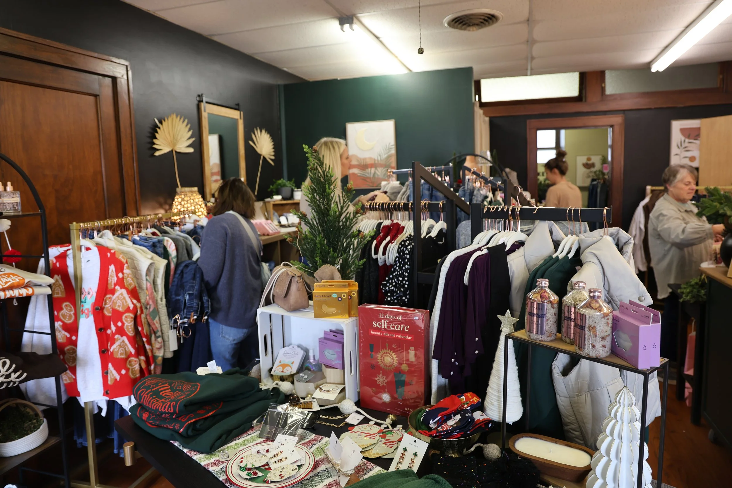 Indoor boutique with racks of clothes, Christmas decorations, and shoppers browsing.