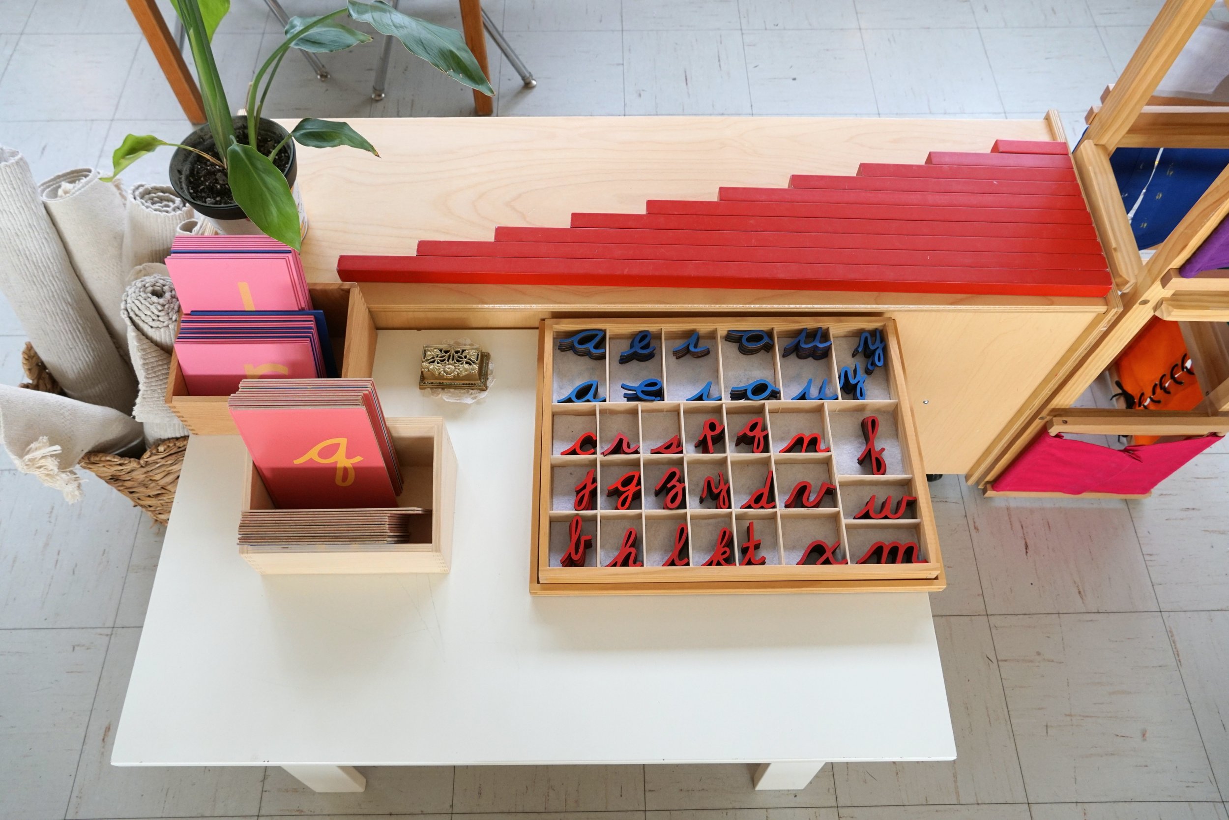 An indoor display with educational materials including letter cutouts, flashcards, a potted plant, and fabric rolls on a white table.