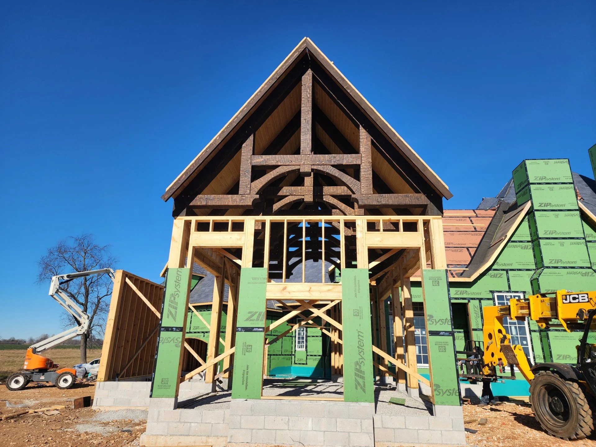 Construction site of a house with wooden framing and green insulation panels, a small waterfall feature inside, and a clear blue sky.