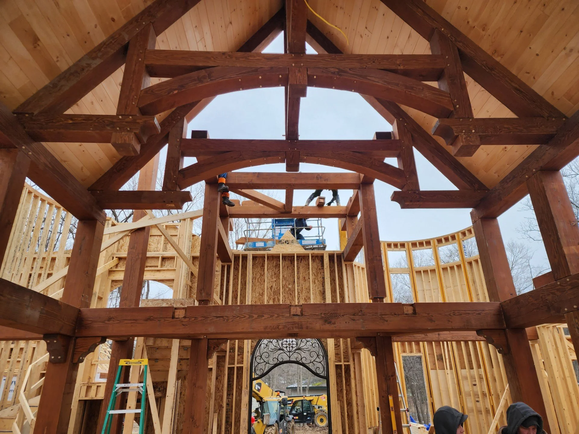 Construction site of a building with wooden framework and a large open archway, workers present, and construction equipment visible.