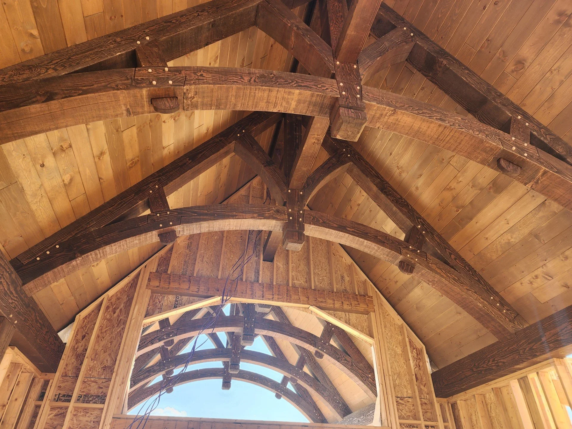 Interior view of a wooden roof structure with multiple beams and arches under construction.