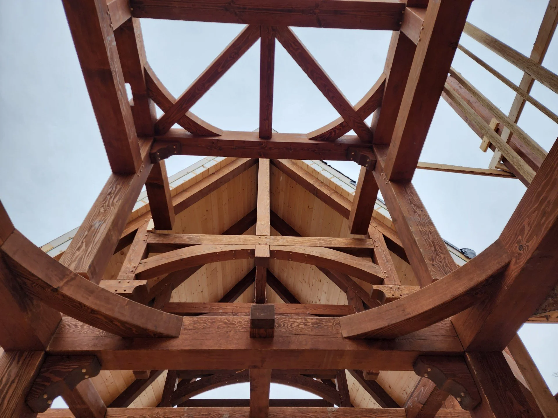 Looking up at the unfinished wooden framework of a building under construction, with a clear sky visible above.