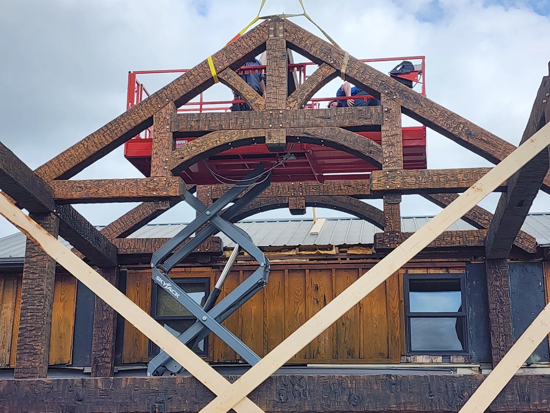 Construction workers on scaffolding inspecting the wooden framework of a building under construction, with cloudy sky background.
