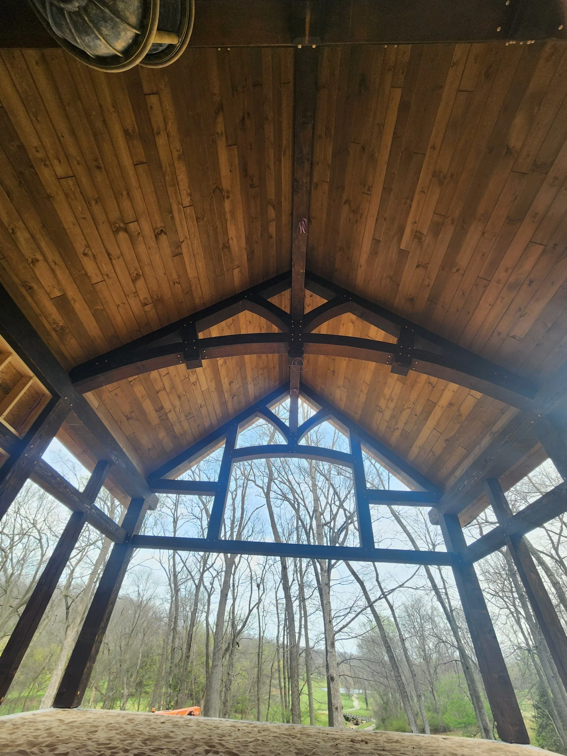 View from inside a wooden structure with a thatched roof, looking out over trees and a landscape with a pathway, in a rural or forested area.