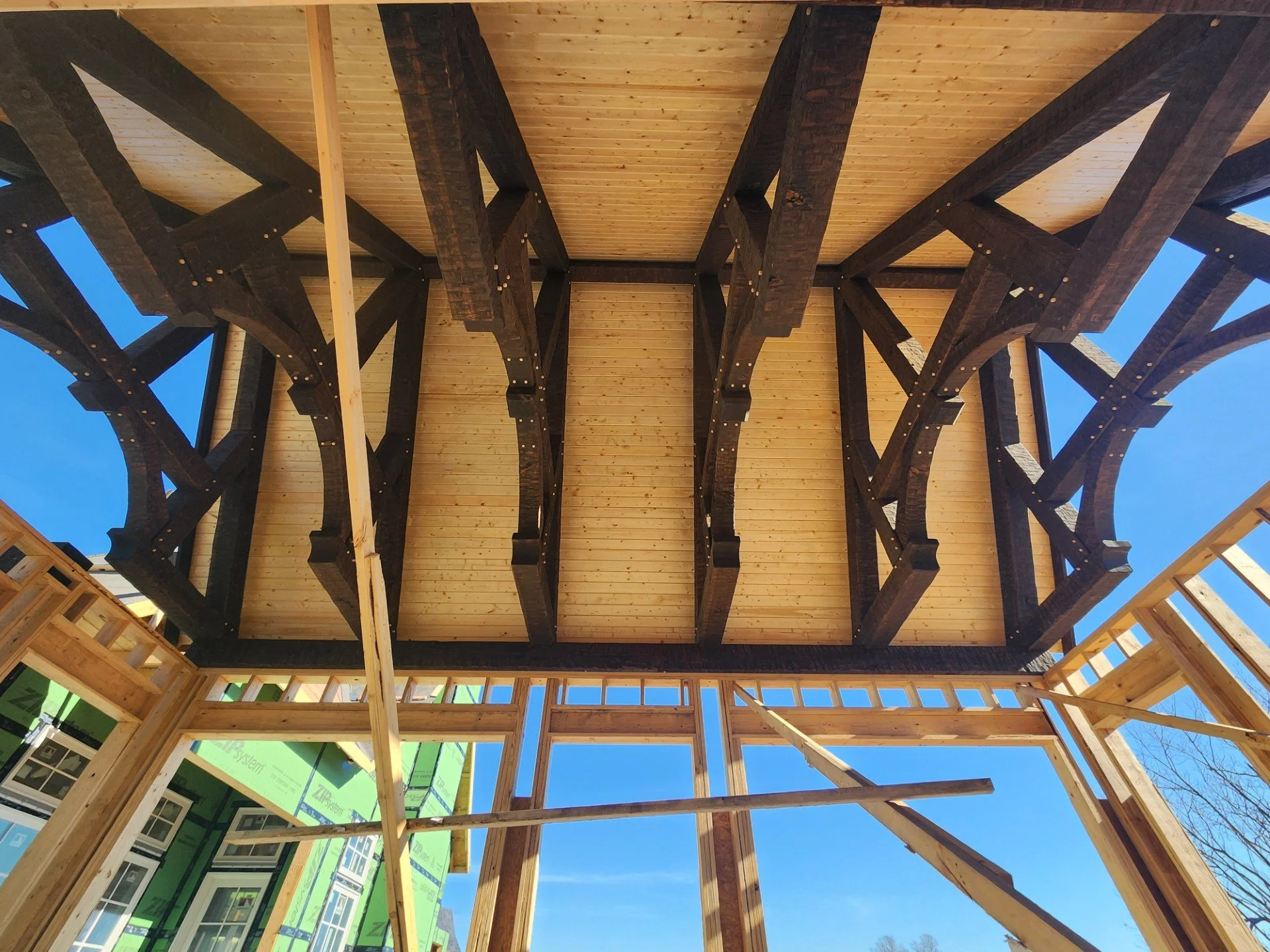 View of the underside of a building under construction, showing wooden beams and framing against a clear blue sky.