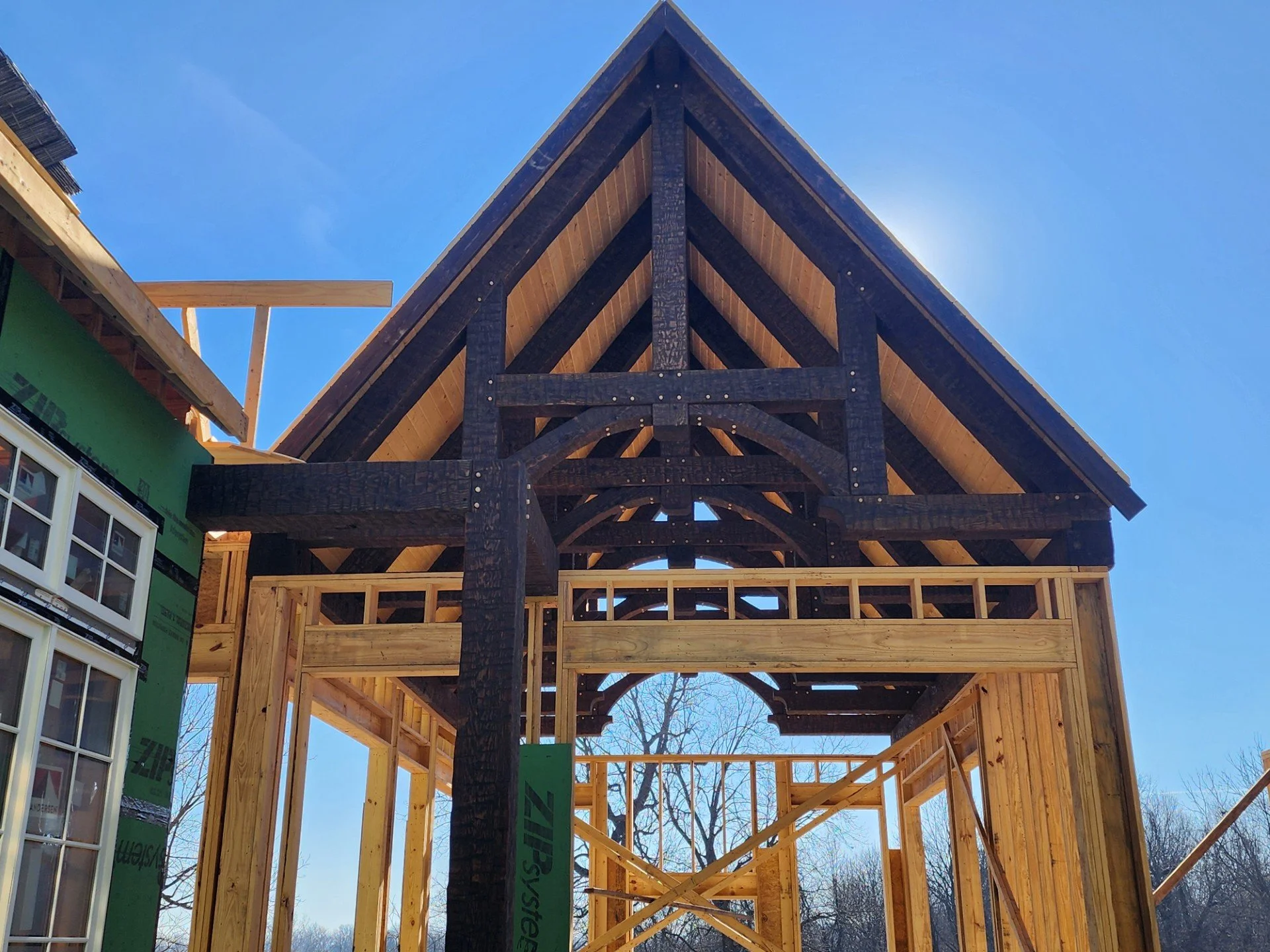 Wood-framed building under construction with exposed roof trusses and scaffolding, blue sky in the background.