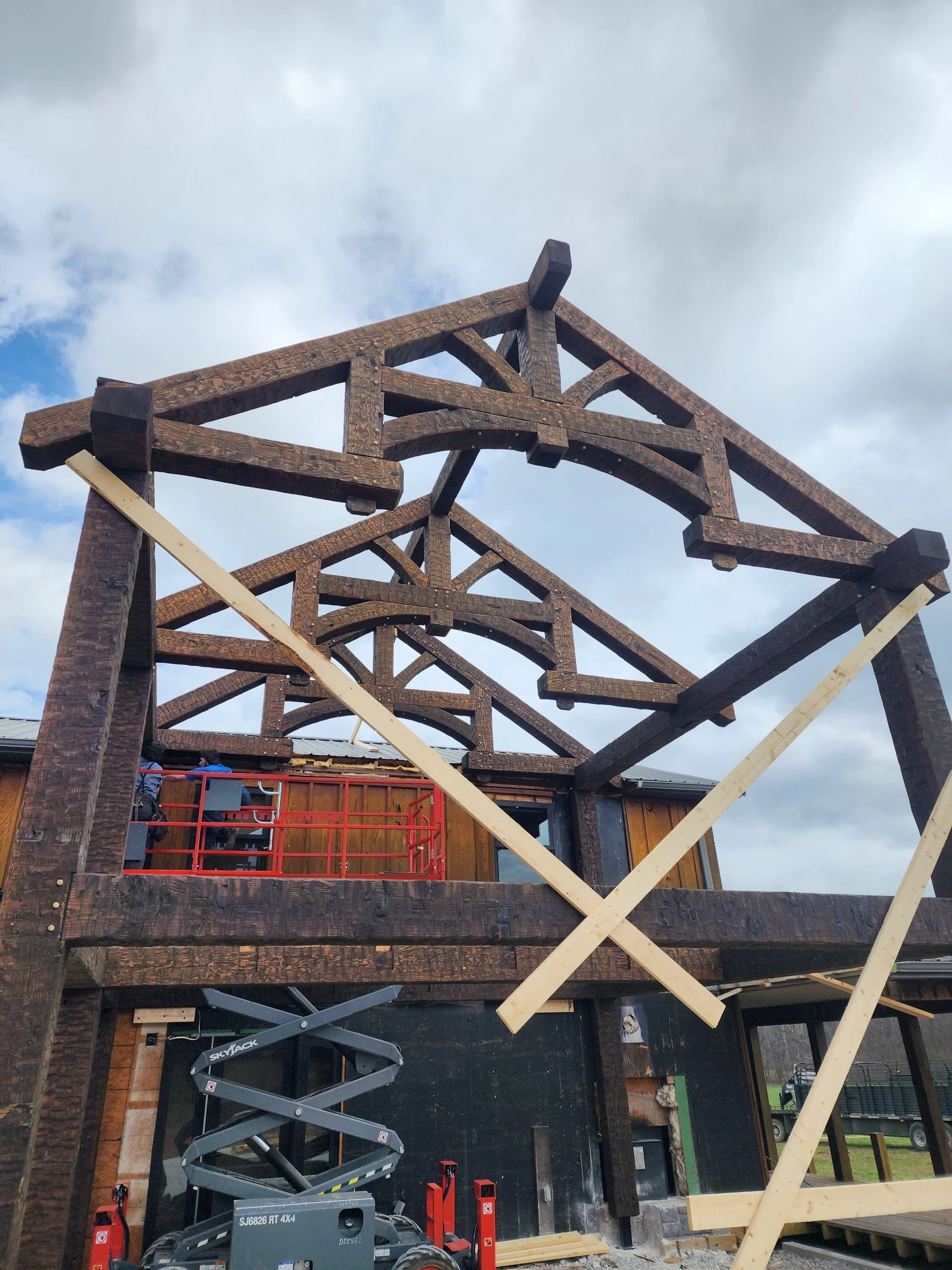 Construction site with a wooden framework of a building under construction, cloudy sky in the background, tools, and equipment visible.
