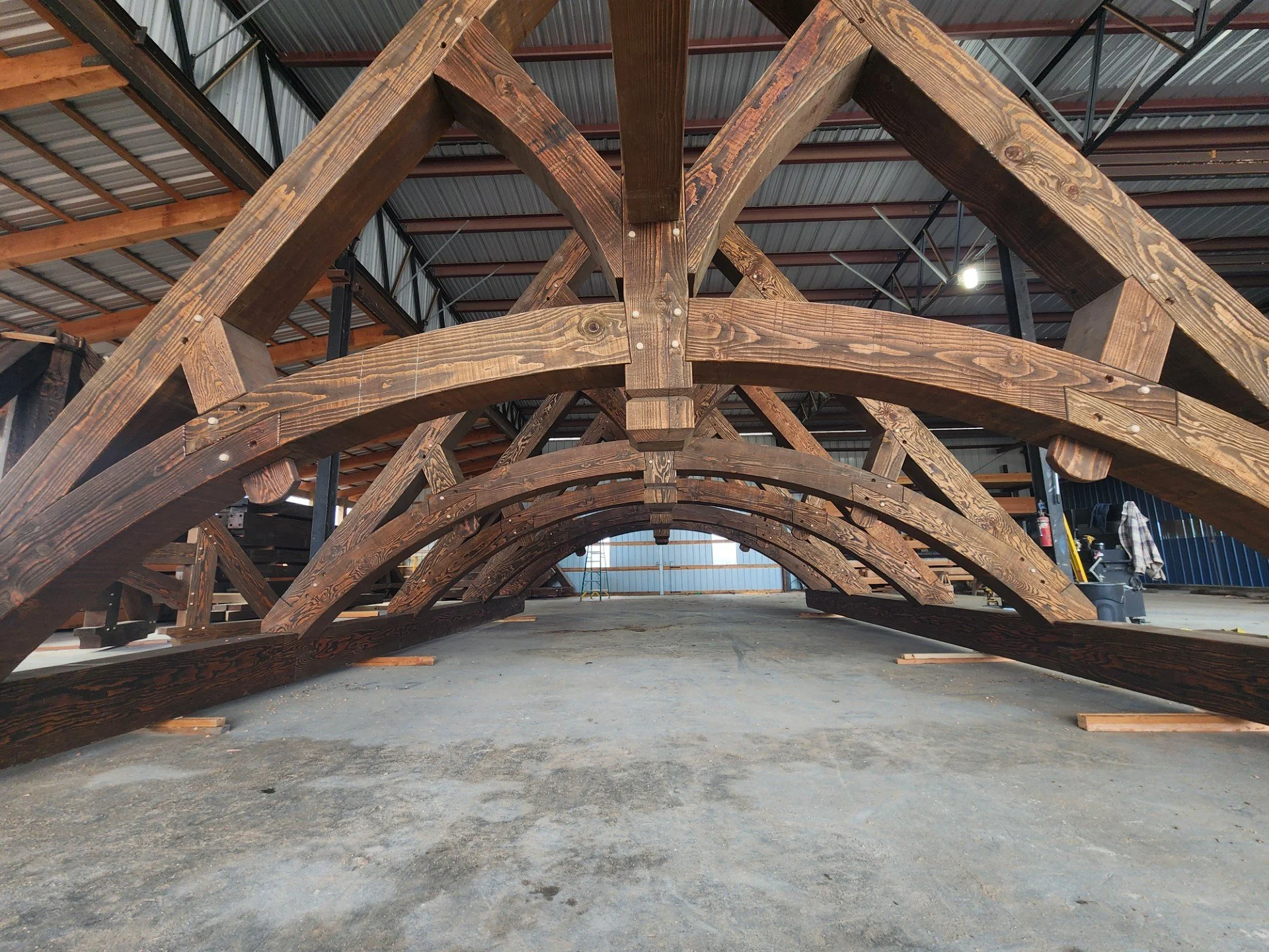 Several large wooden arches under construction inside a warehouse or workshop.