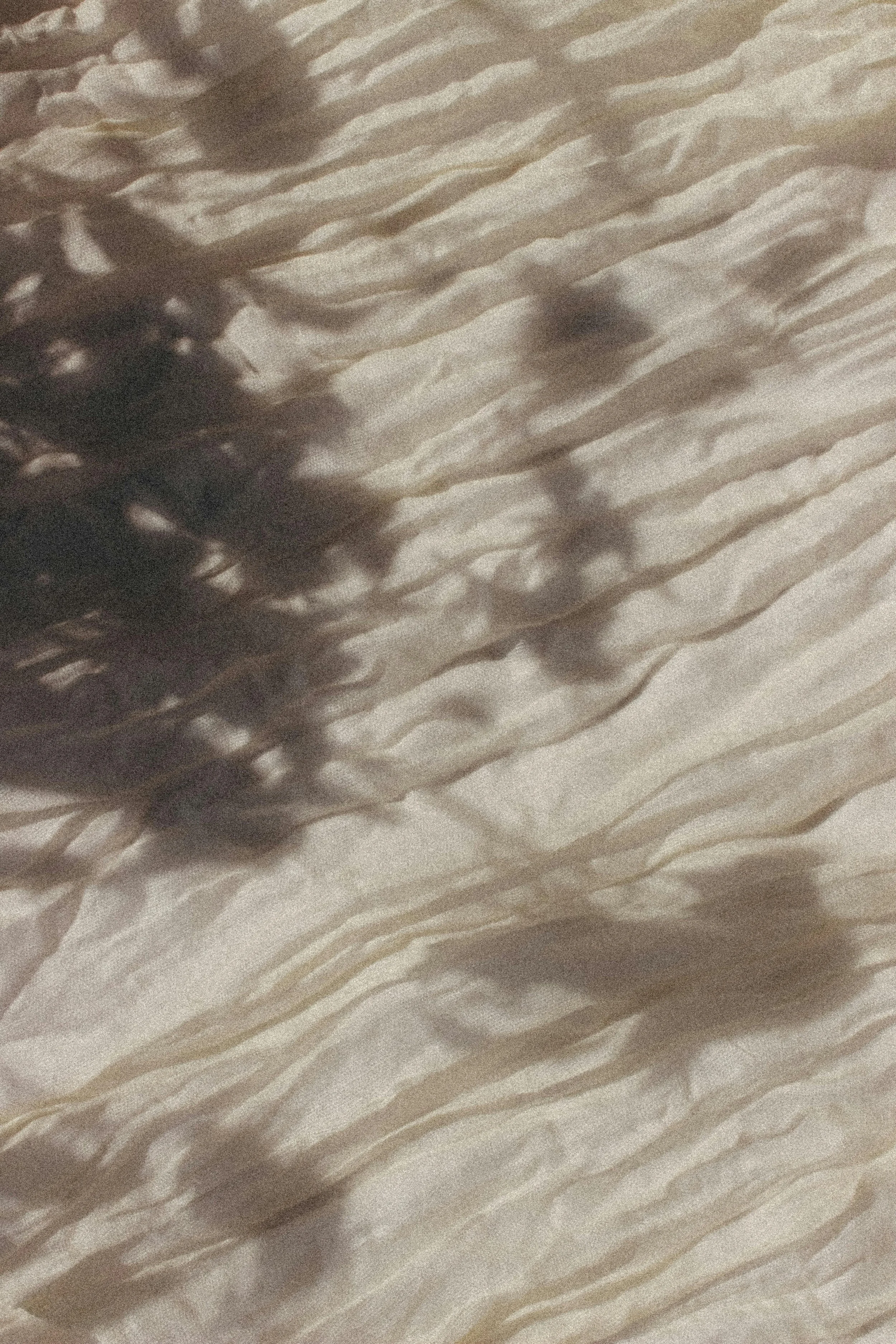 Close-up of textured fabric with shadows of leaves cast on it.