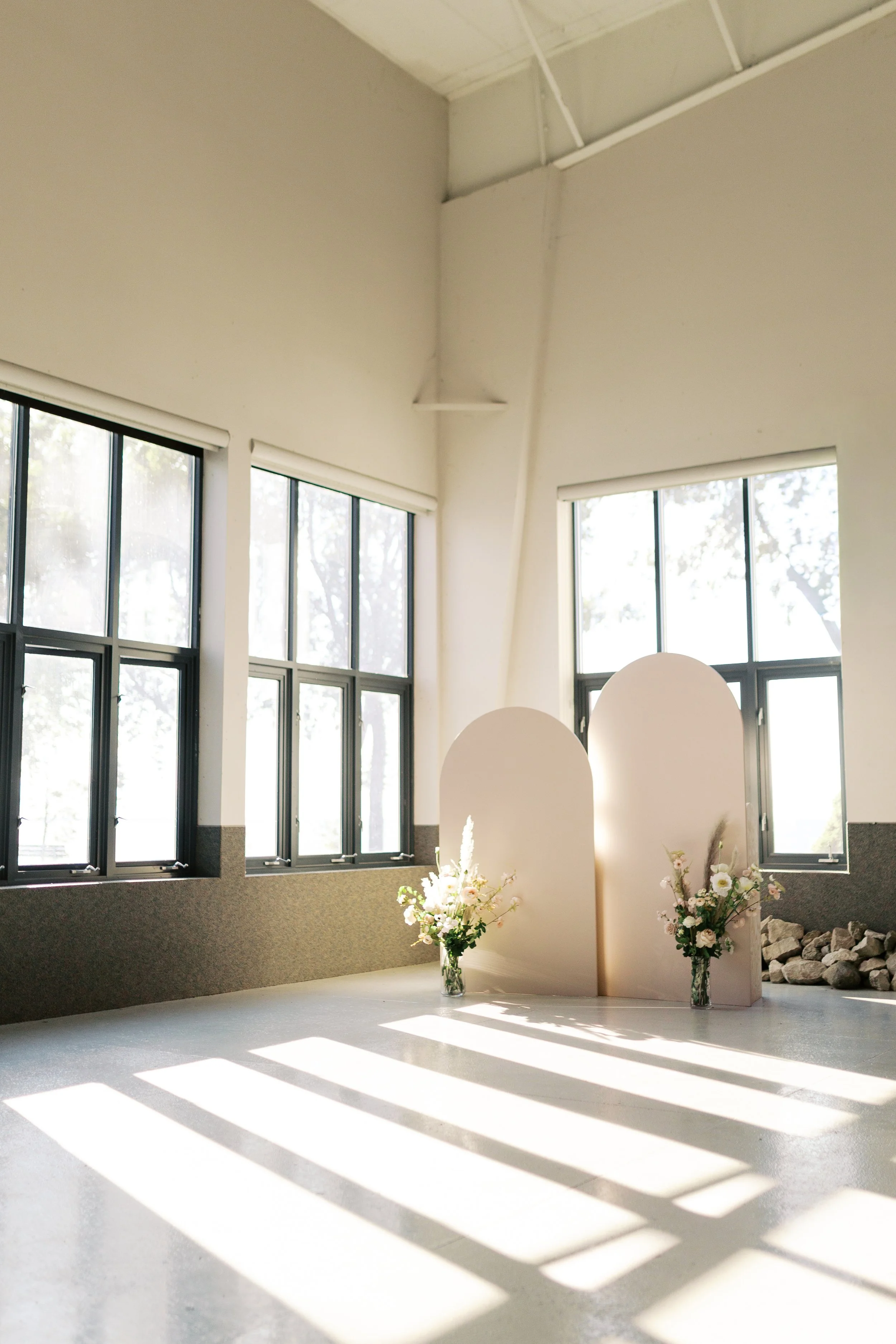 Sunlit indoor space with large windows, a standing room divider, and two floral arrangements in vases.