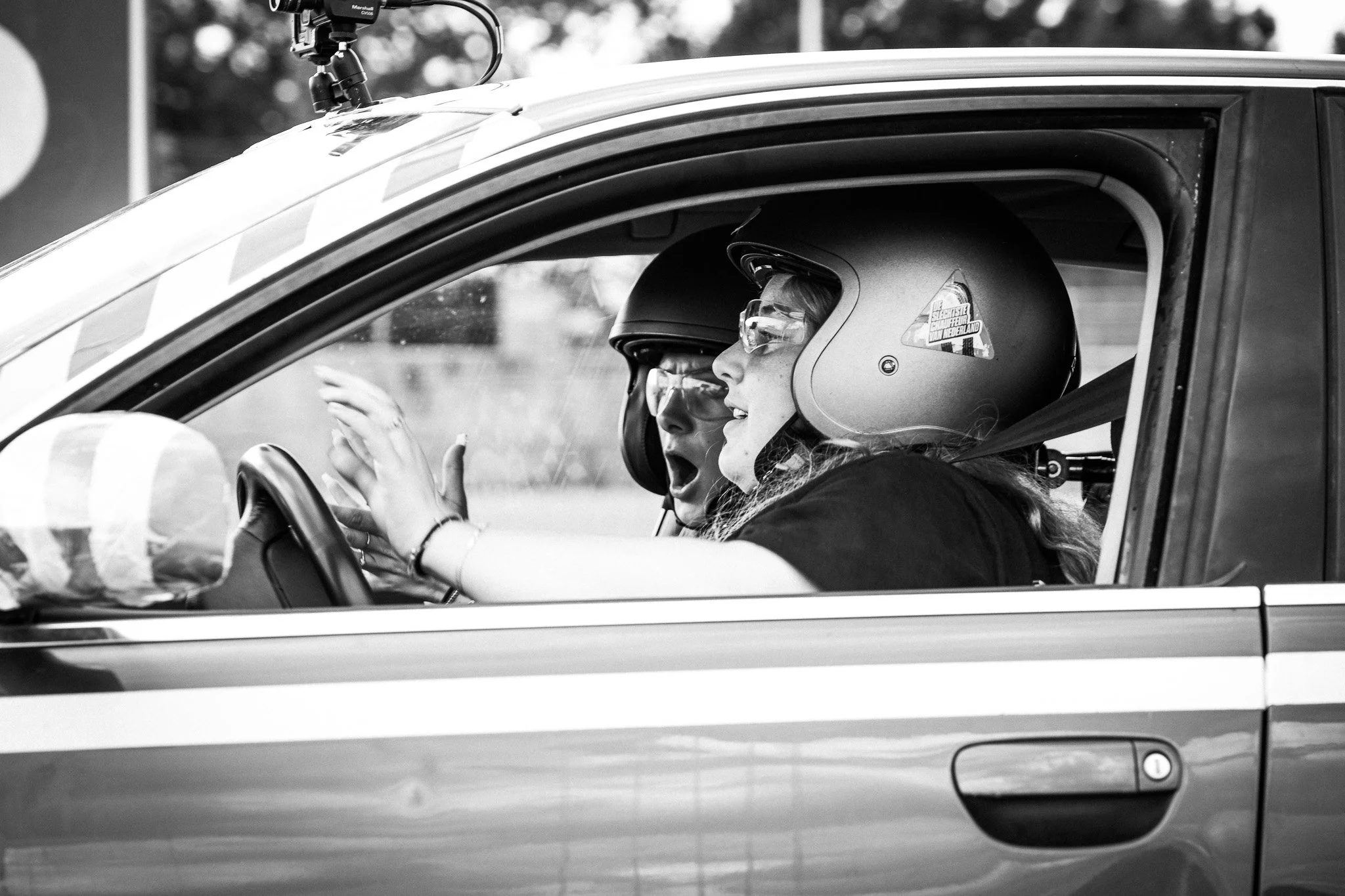 Twee vrouwen dragen helmen en zitten in een voertuig, mogelijk een raceauto, klaar voor een race of oefening.