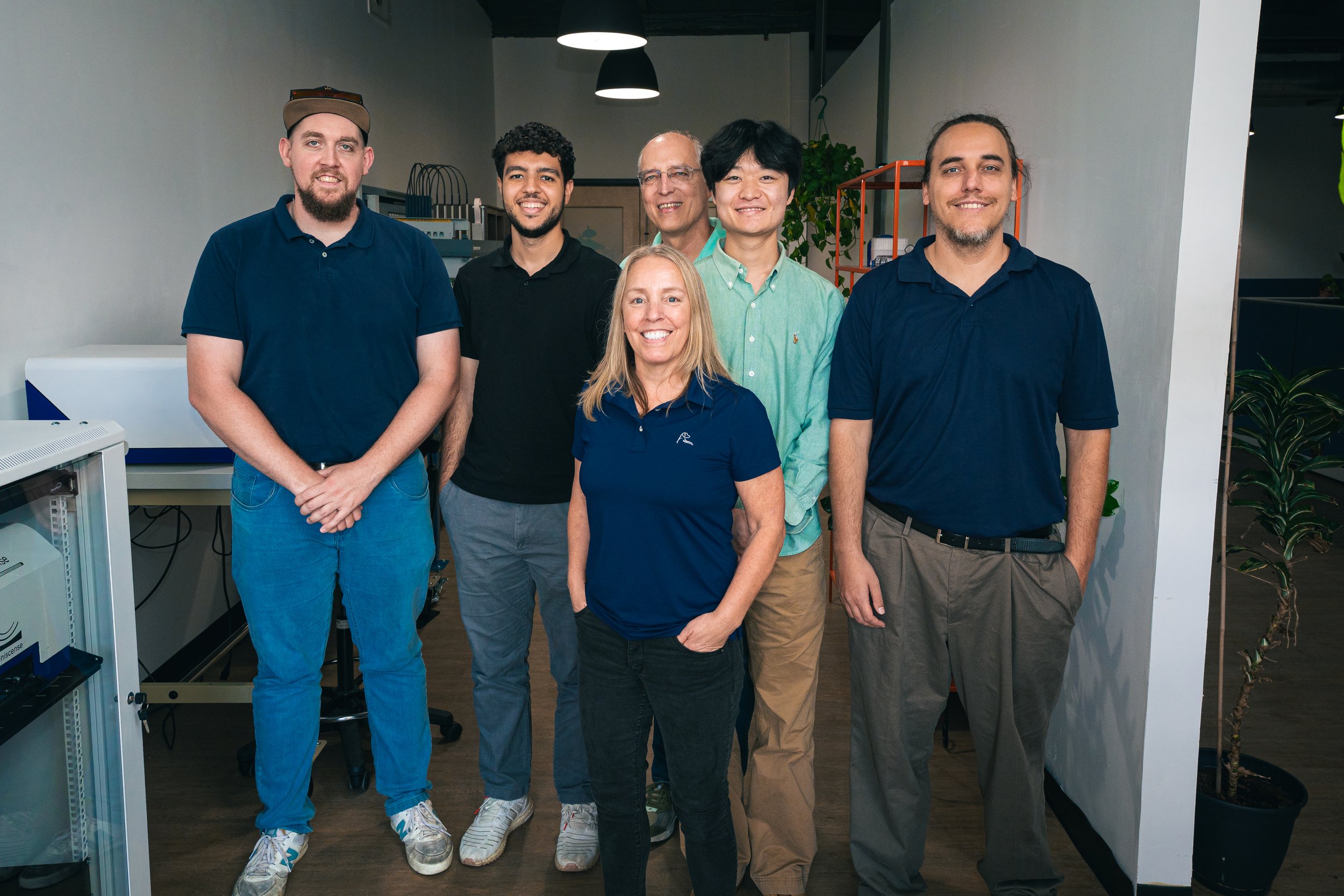 Group of six people standing together in an office, smiling at the camera.