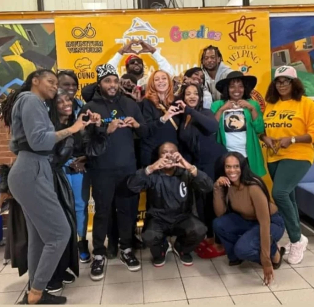 Group of people smiling and making heart shapes with their hands in front of a colorful banner.