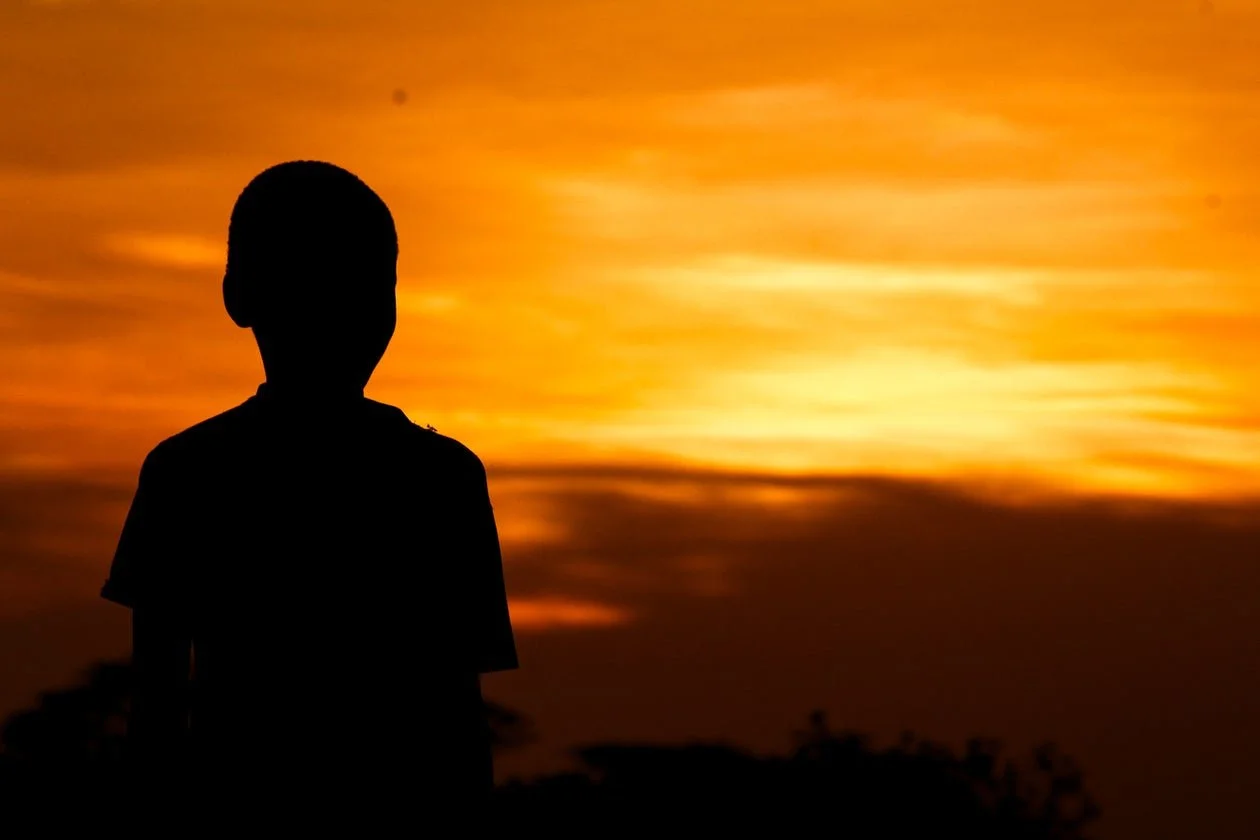 Silhouette of a child against a sunset sky with orange and yellow clouds.