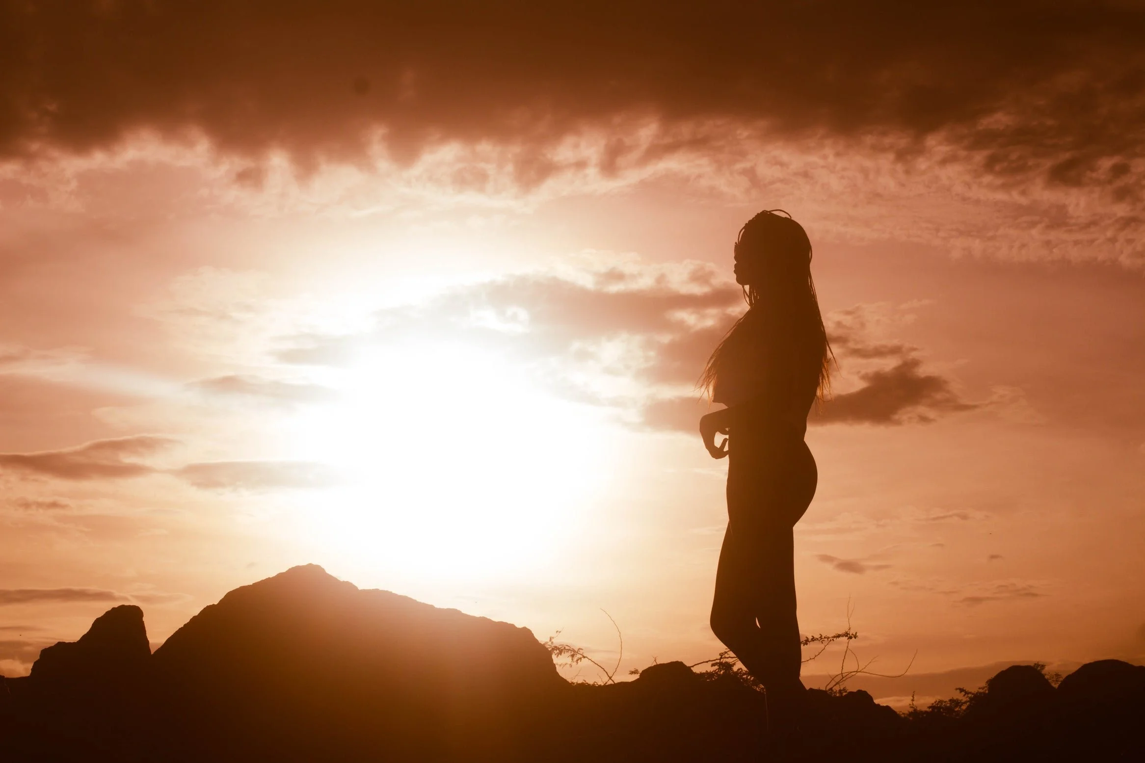 Silhouette of a woman standing on rocks during sunset with a cloudy sky in the background.
