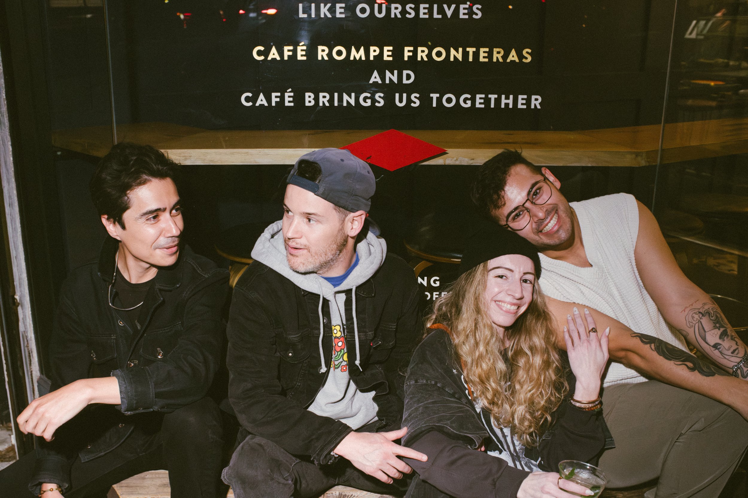 A group of five friends sitting together at a bar or restaurant, smiling and enjoying each other's company.