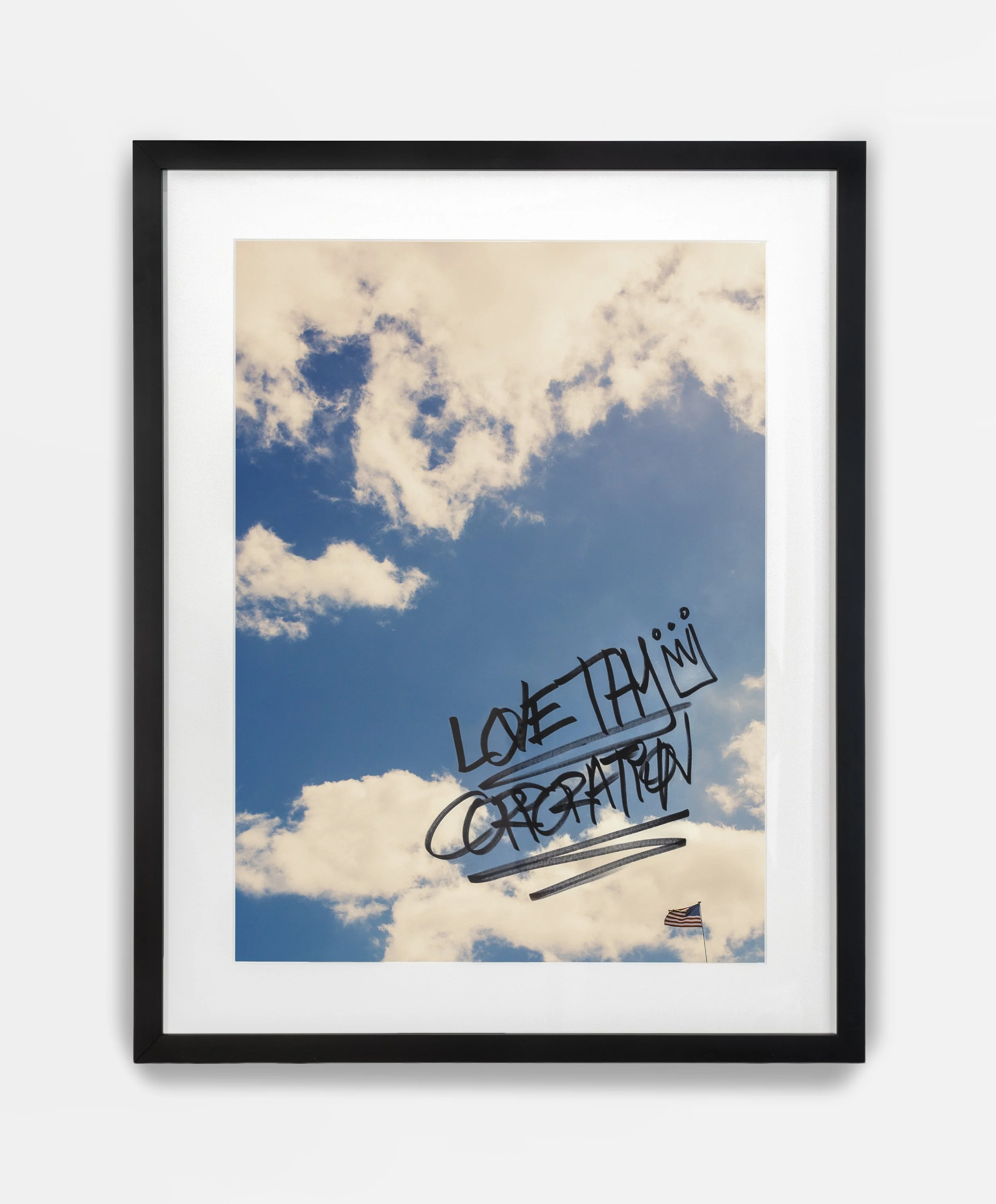 A framed picture of a blue sky with white clouds, with handwritten text on it that says 'LOVE THIS' and 'GRATITUDE.' An American flag is visible in the bottom right corner.