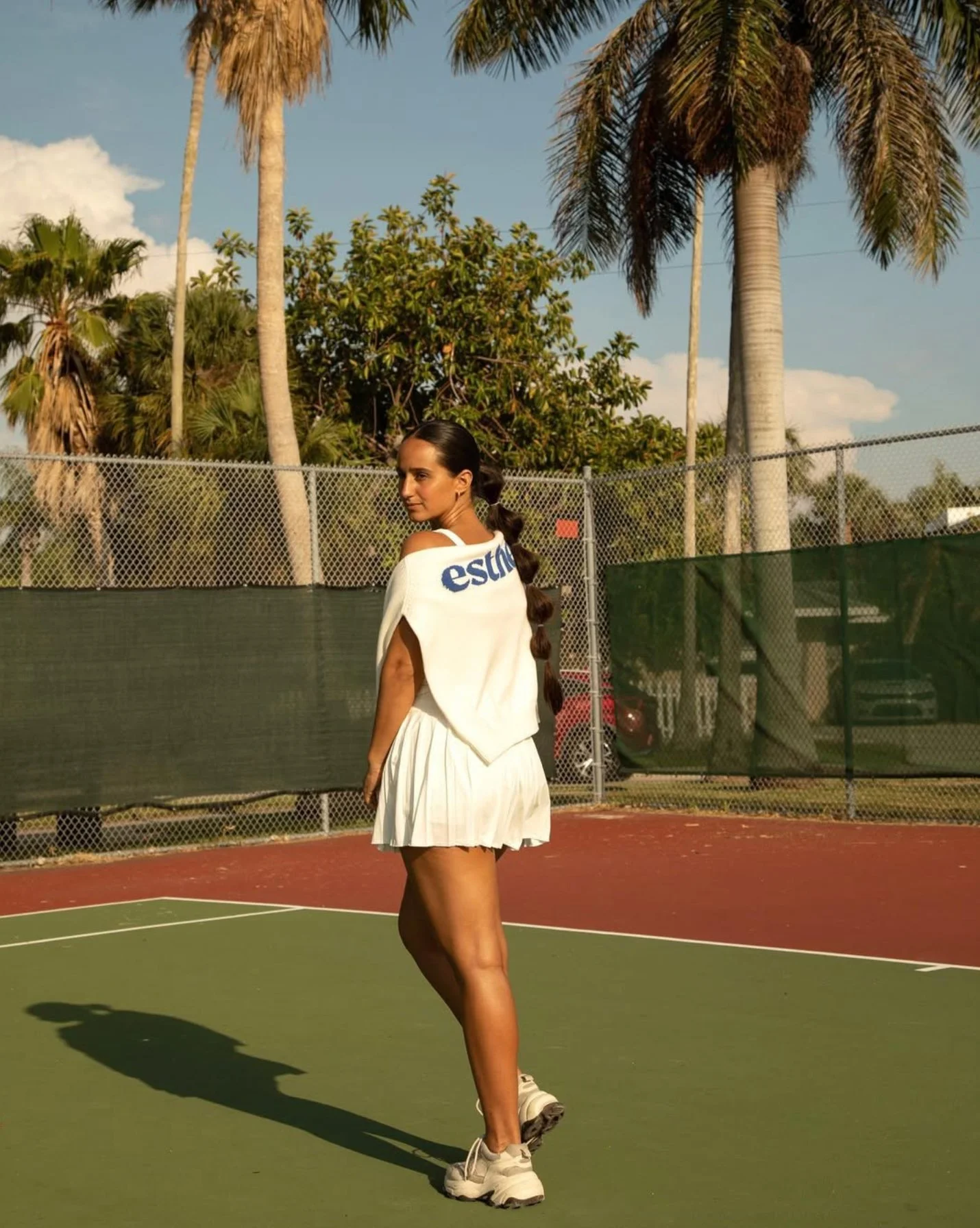 Woman standing on tennis court modeling clothes.