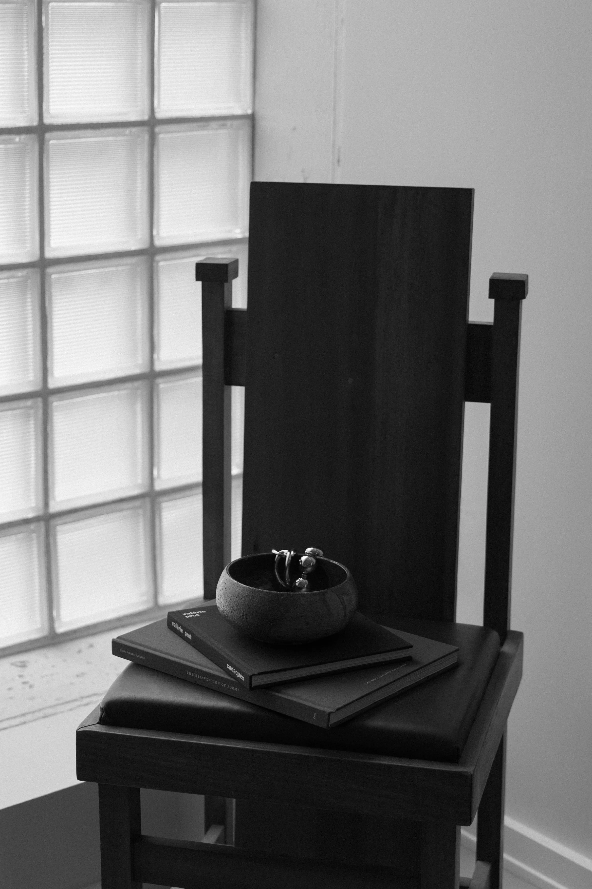 Black and white high-back chair with ceramic bowl and books on it.