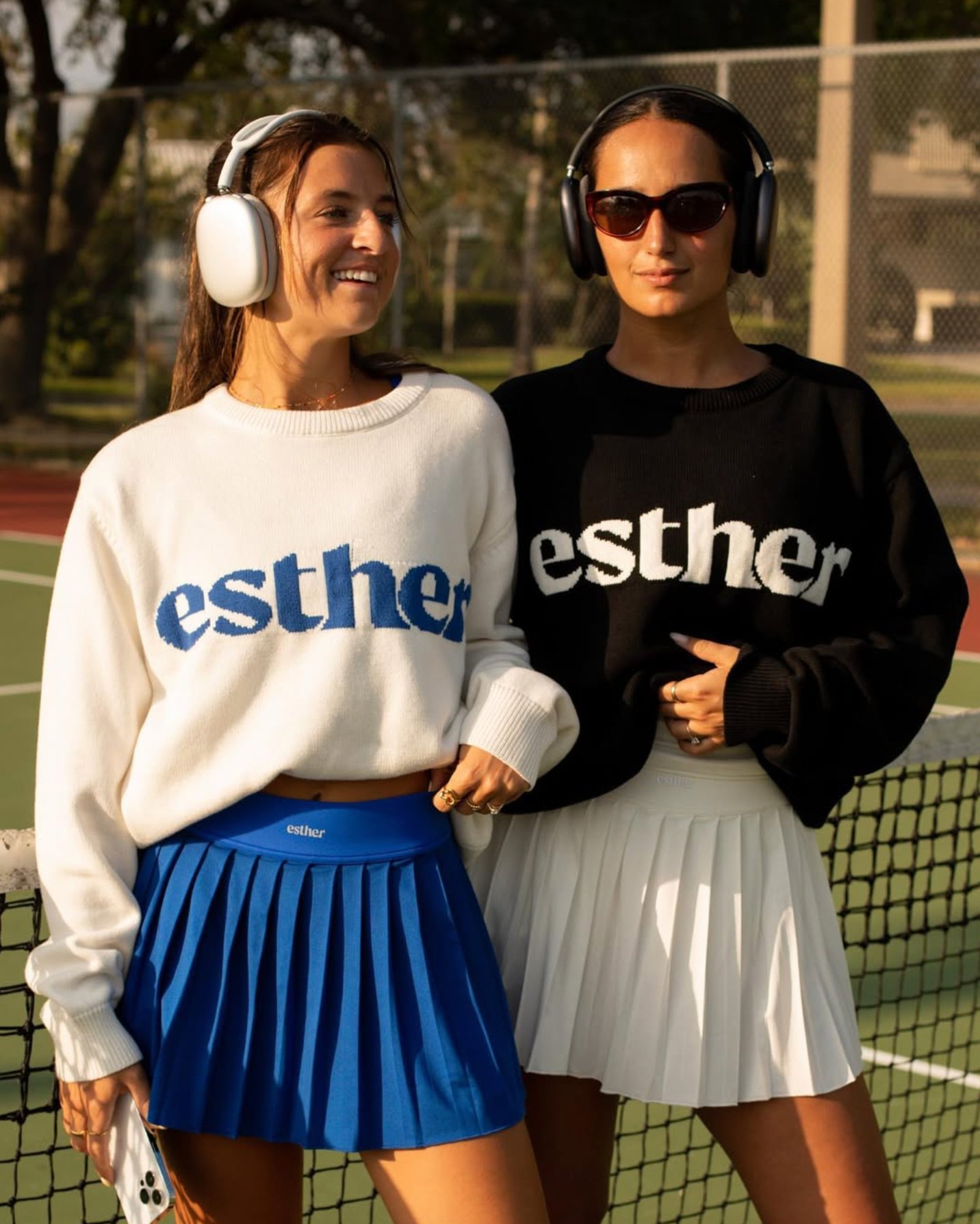 Women standing on tennis court modeling clothes.