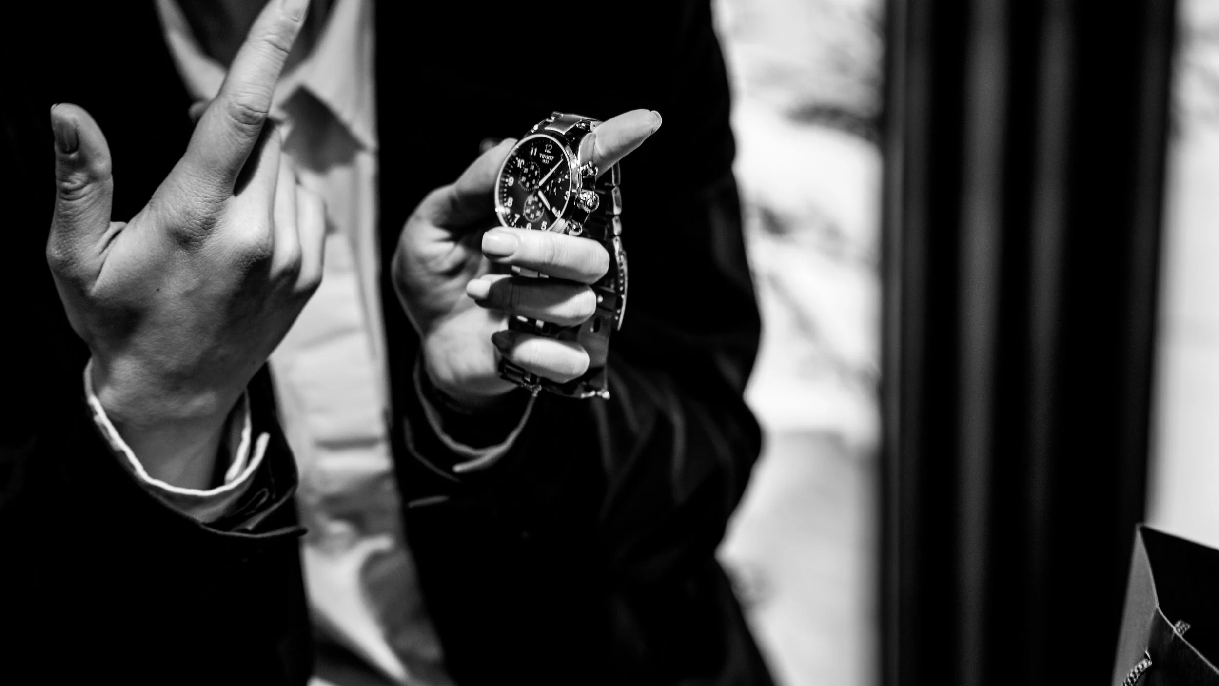 A woman is holding a wristwatch in her hand while making a gesture with her other hand. The photo is in black and white.