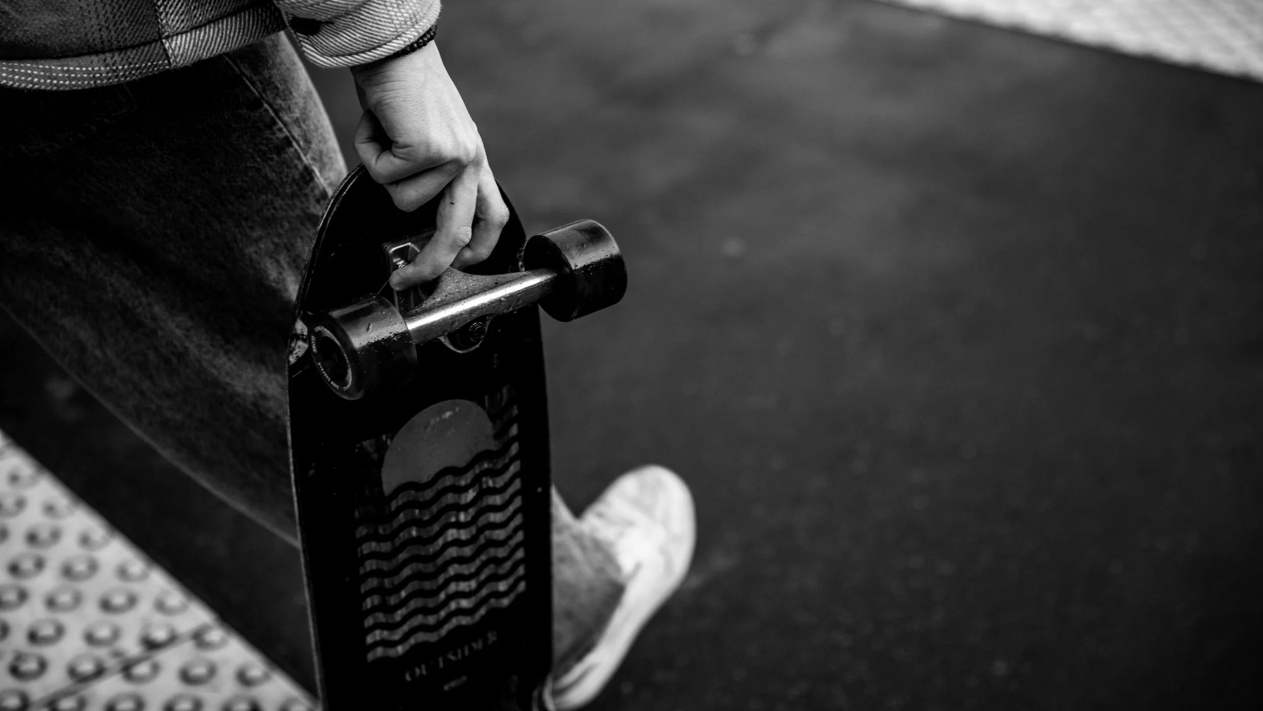 A person sitting on a skateboard on a textured surface, holding the skateboard's tail.
