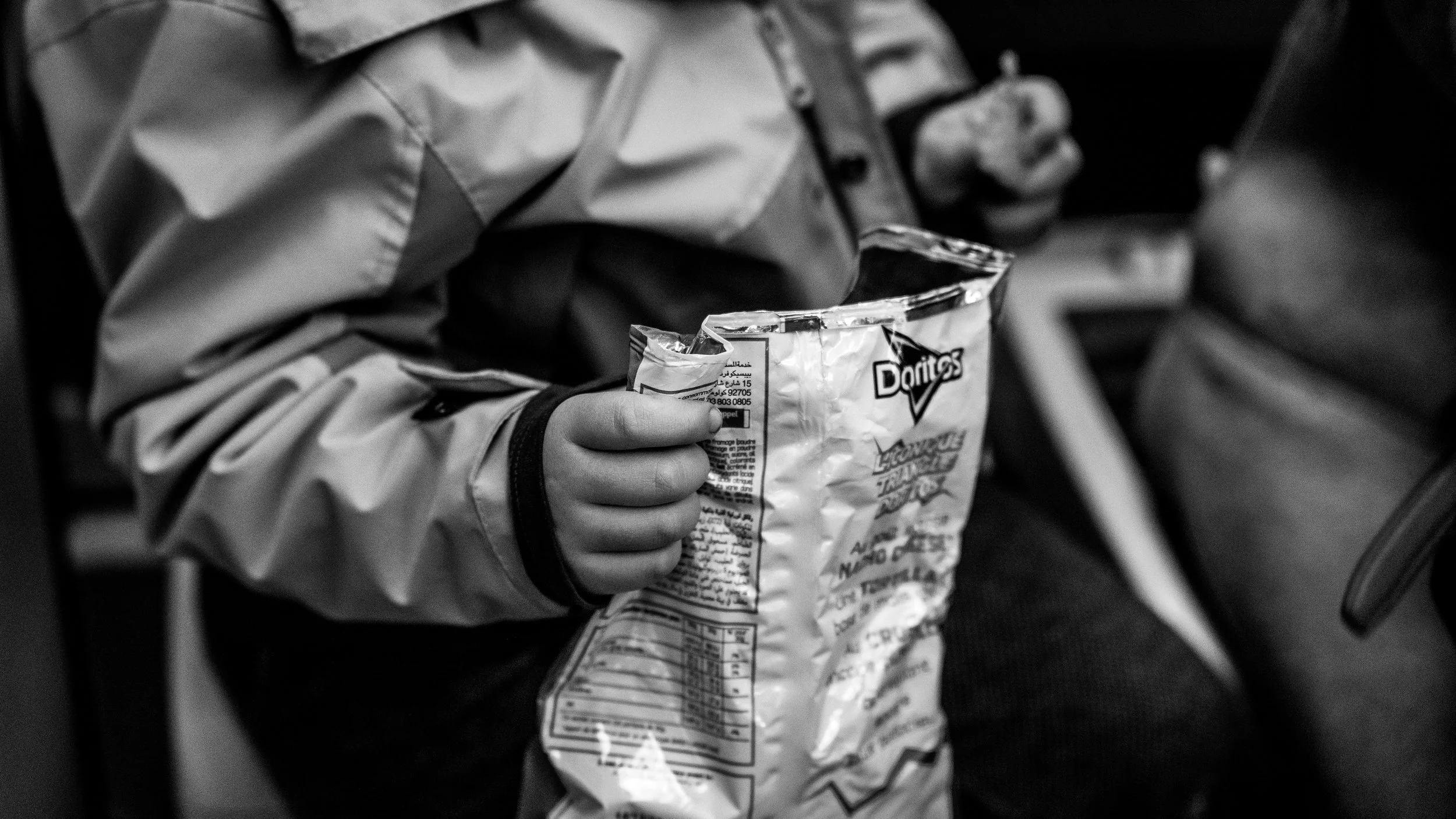 A person in a jacket holding an open bag of Doritos chips in black and white.