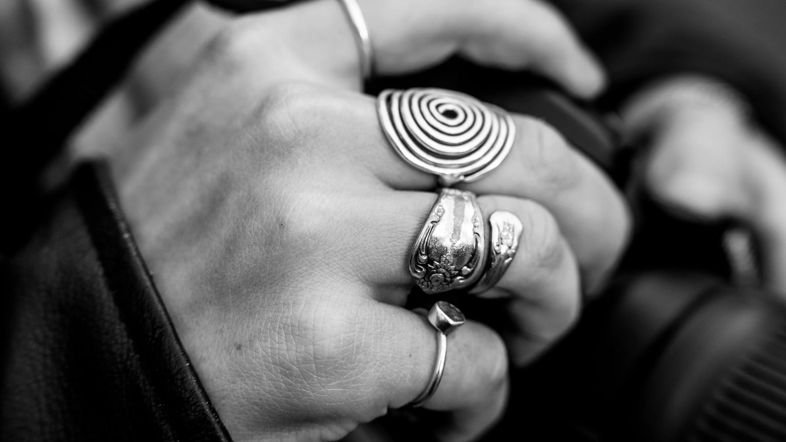 Close-up of a person's hand wearing multiple rings, including one with a spiral pattern, in black and white.