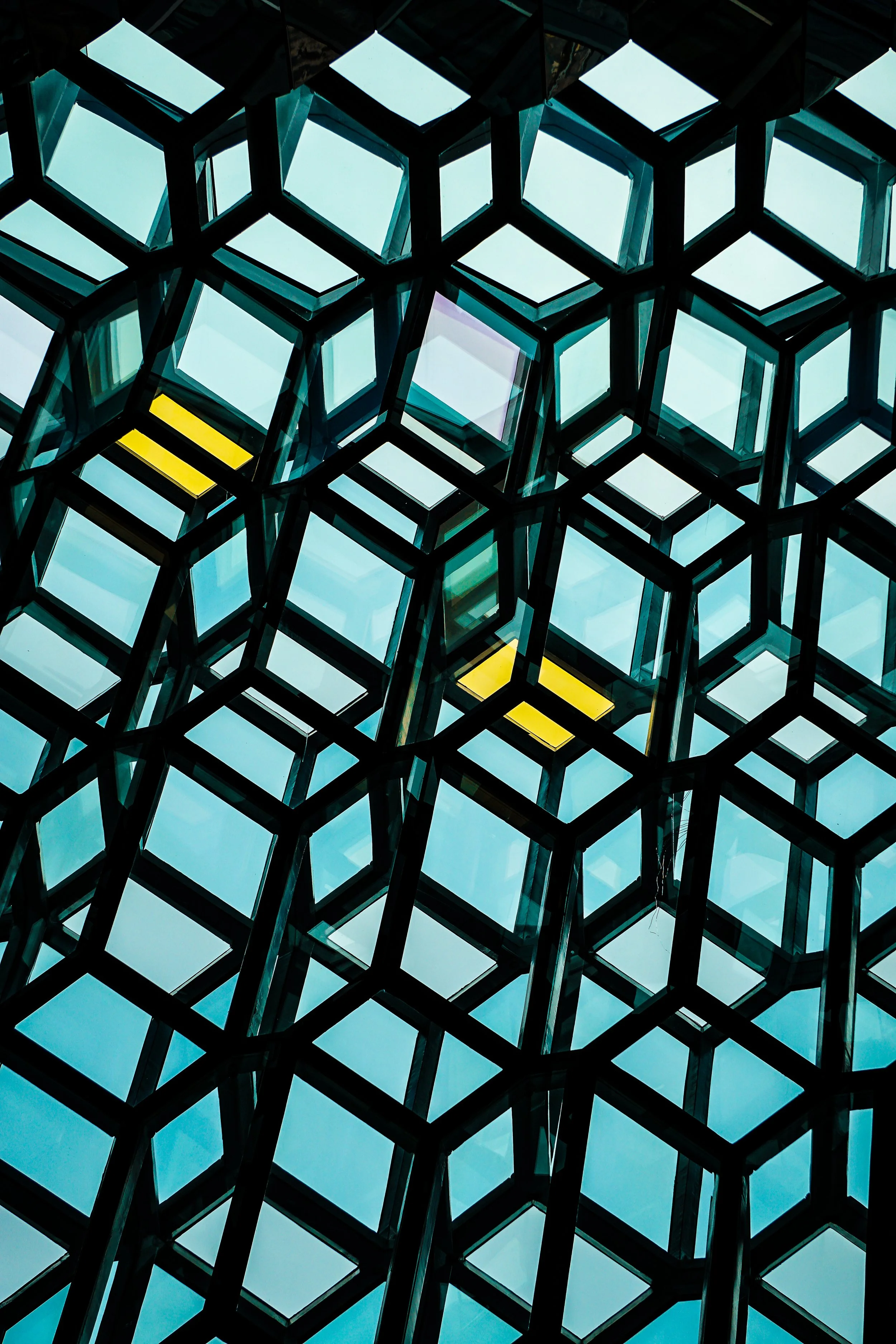 Close-up view of a modern building's glass facade with a geometric pattern of hexagonal and square windows, some of which have yellow blinds.